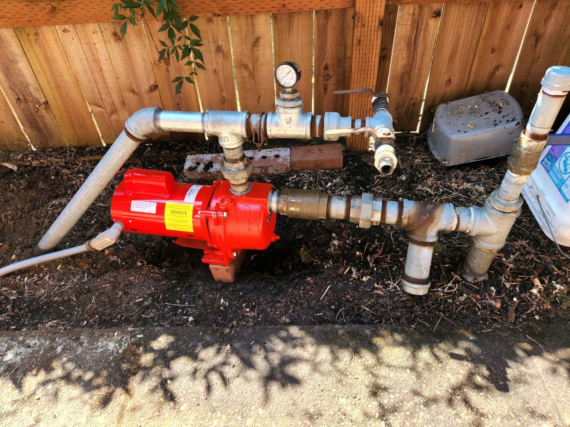 A red water pump is sitting on the ground next to a wooden fence.