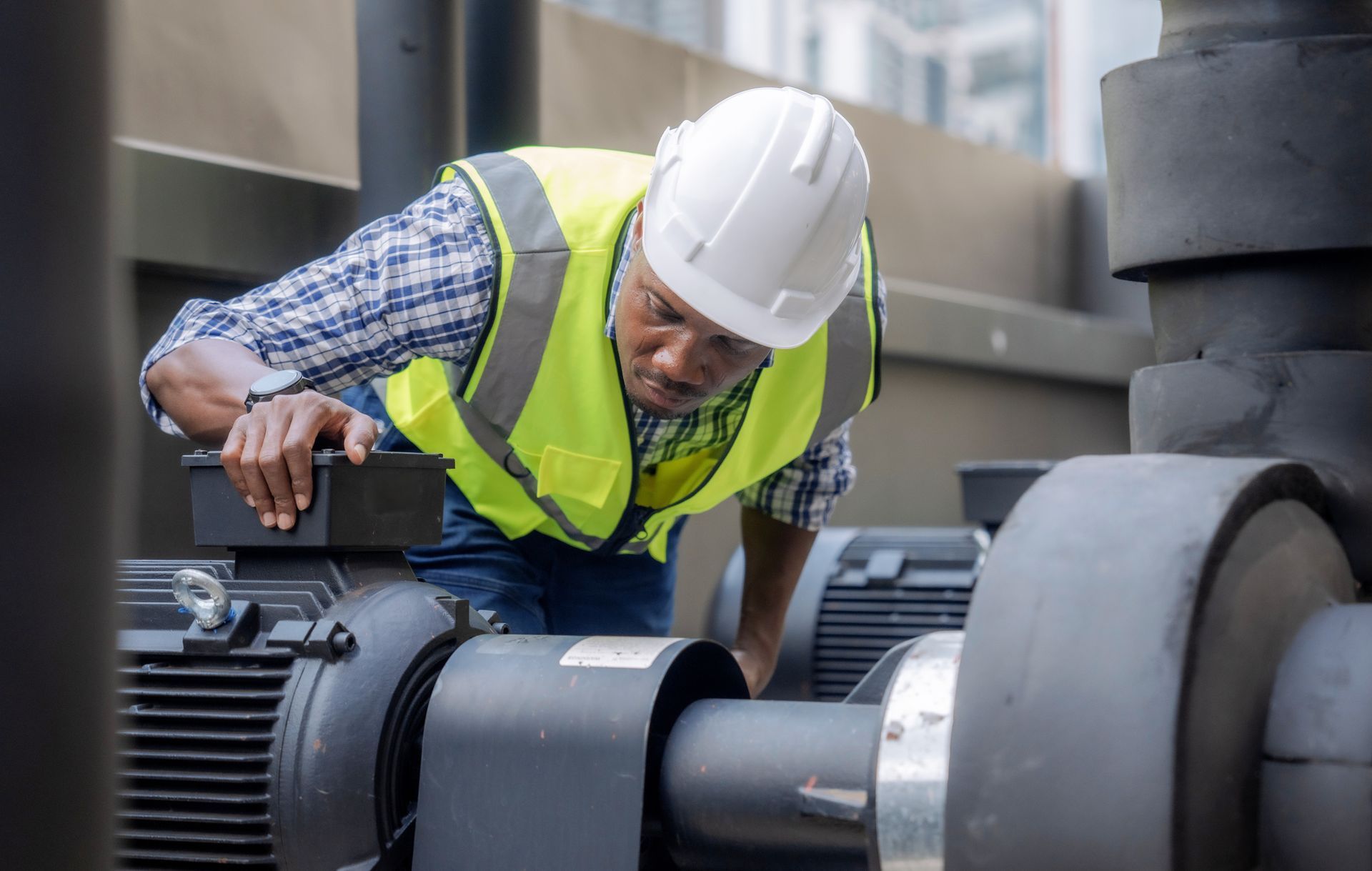 A man wearing a hard hat and safety vest is working on a machine.