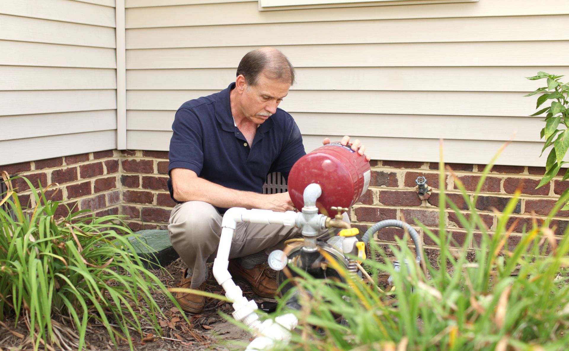 A man is working on a water pump outside of a house.