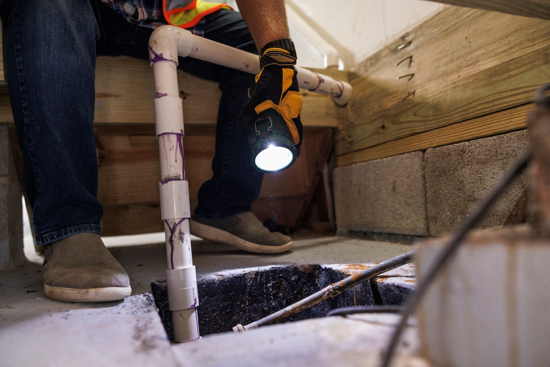 A man with gloves is checking a sump pit with a flashlight. A man with gloves is checking a sump pit with a flashlight.