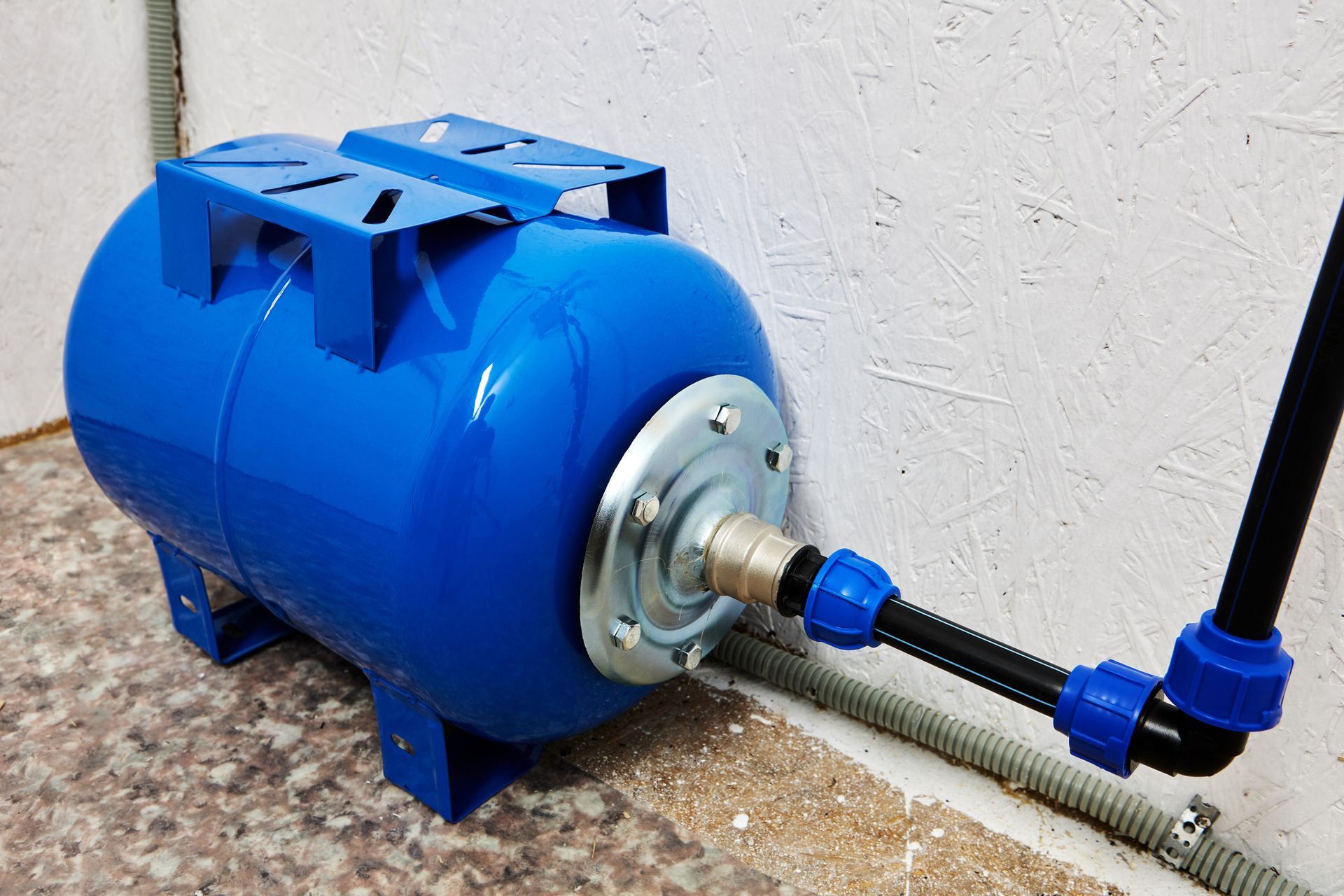 A blue water tank is attached to a pipe on the side of a wall.