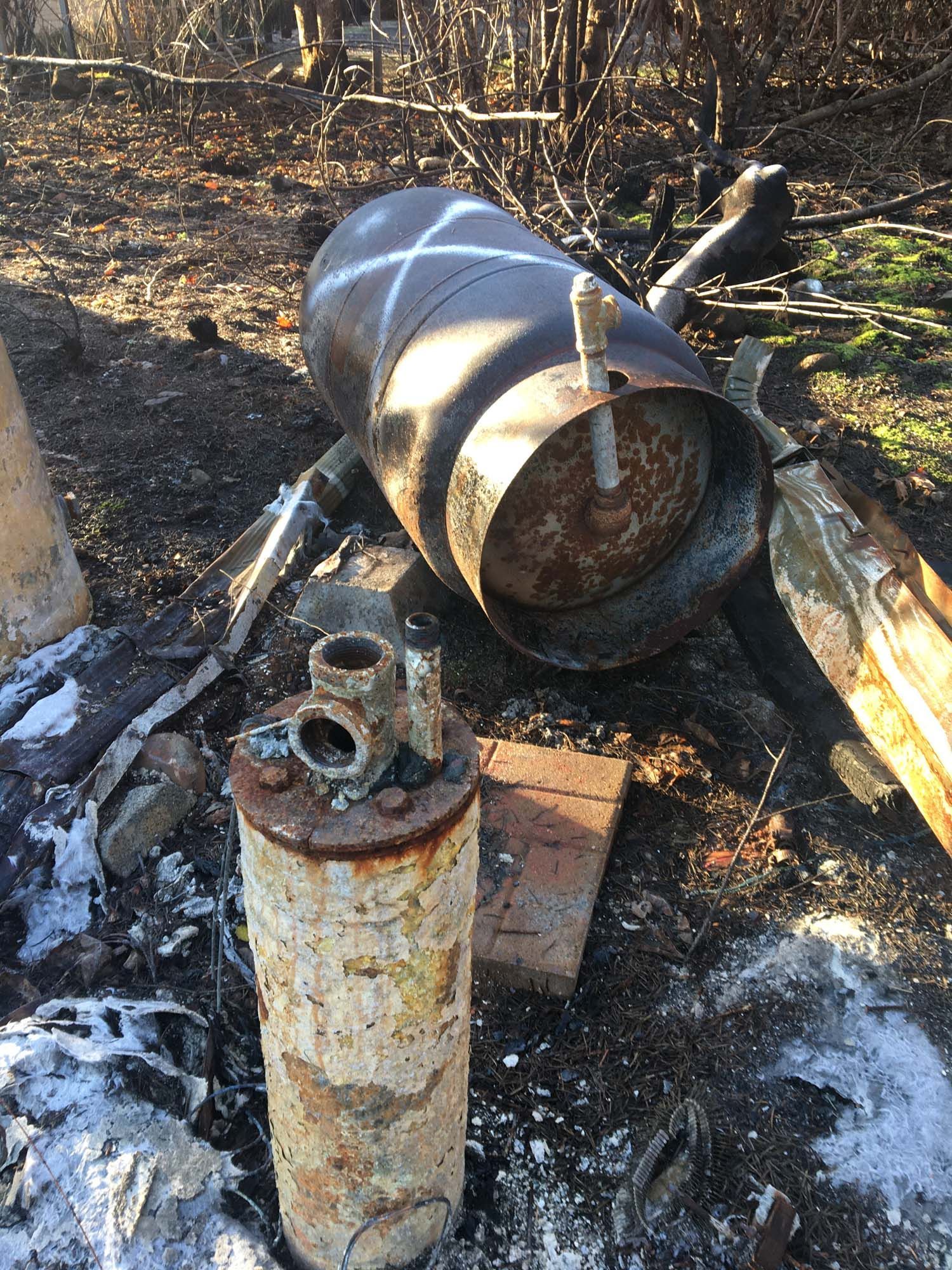 A large rusty barrel is sitting on the ground next to a smaller barrel.
