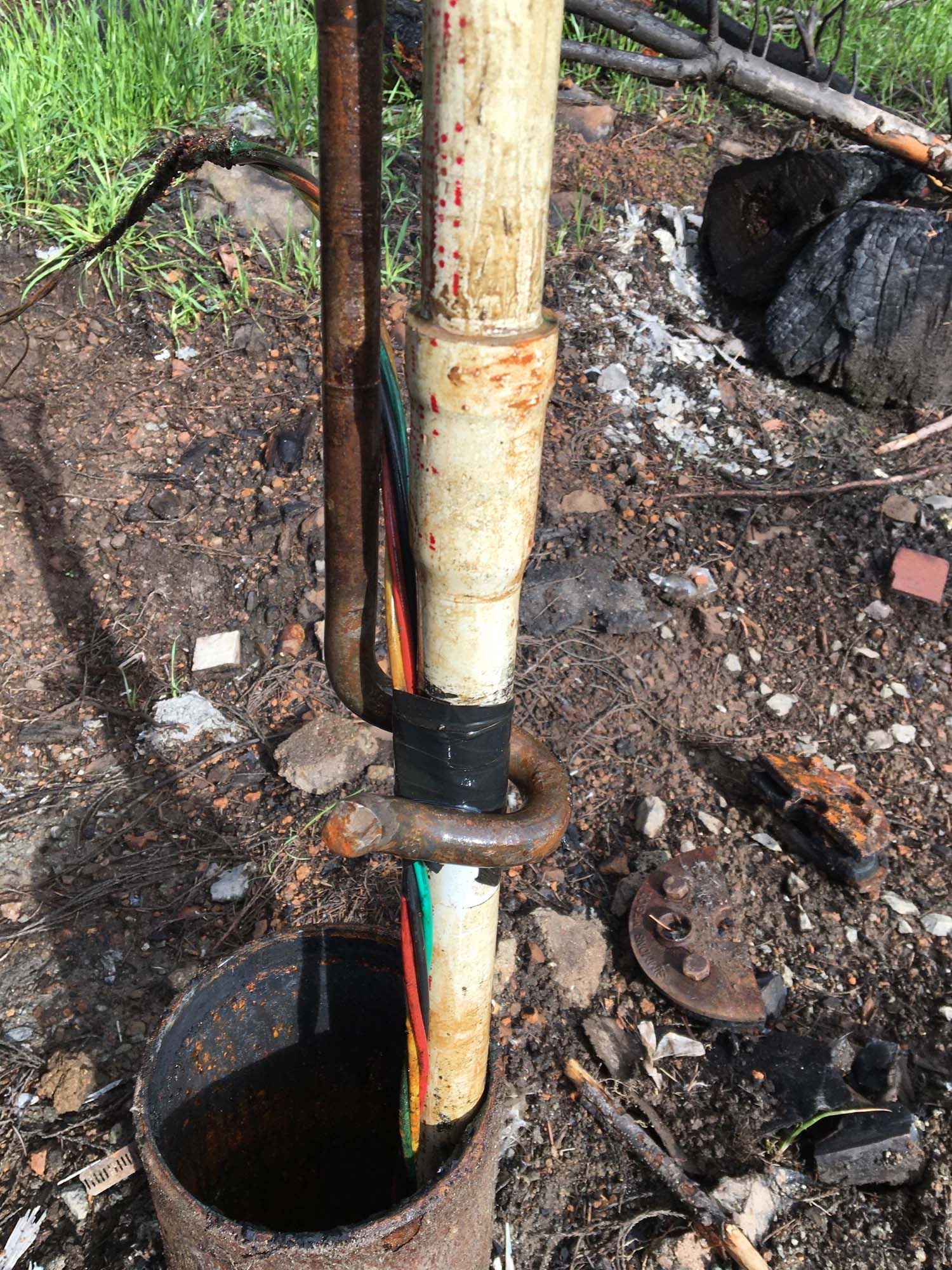 A snake is sticking out of a hole in the ground next to a pipe.