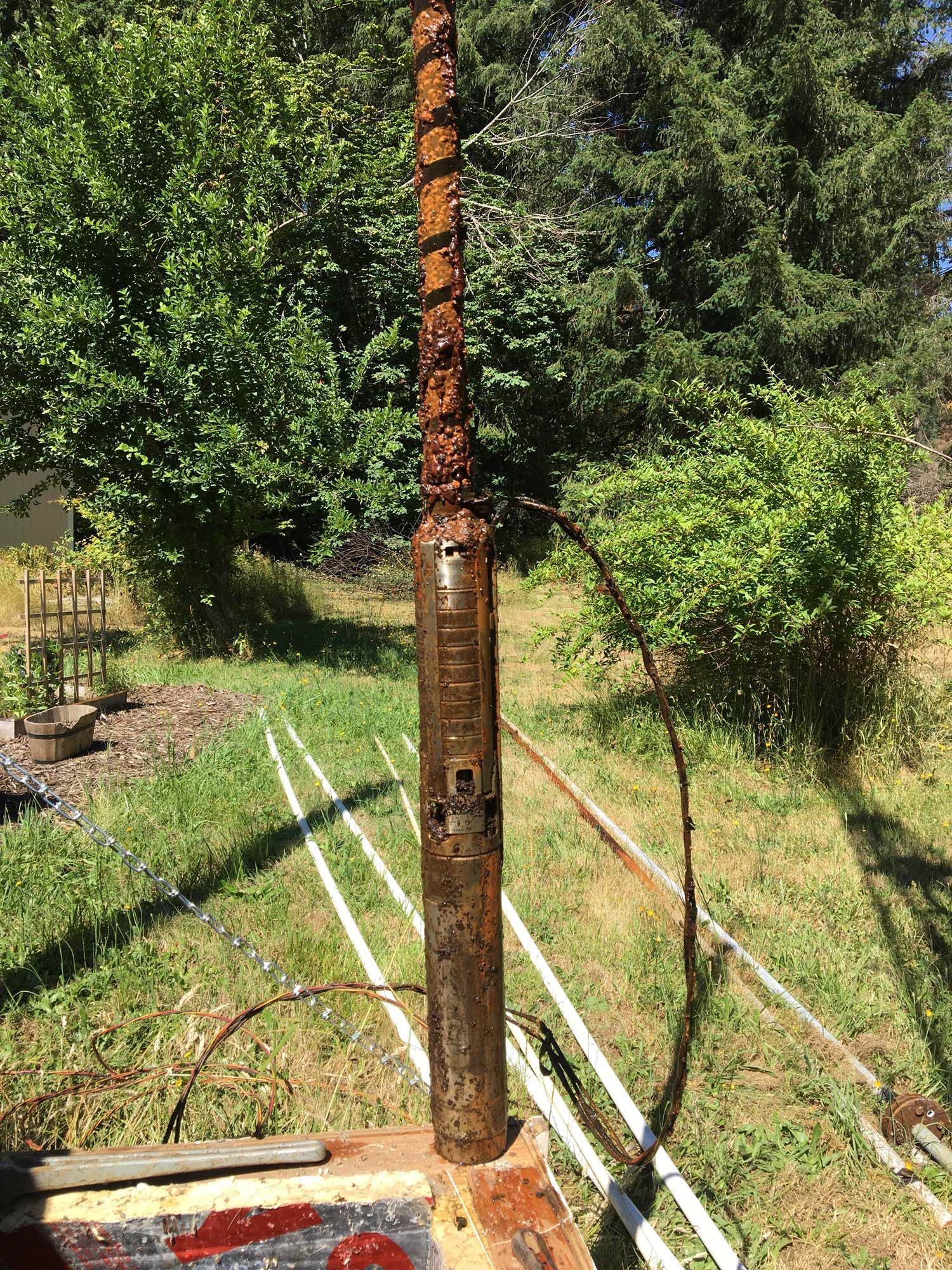 A rusty water pump is sitting in the middle of a grassy field.