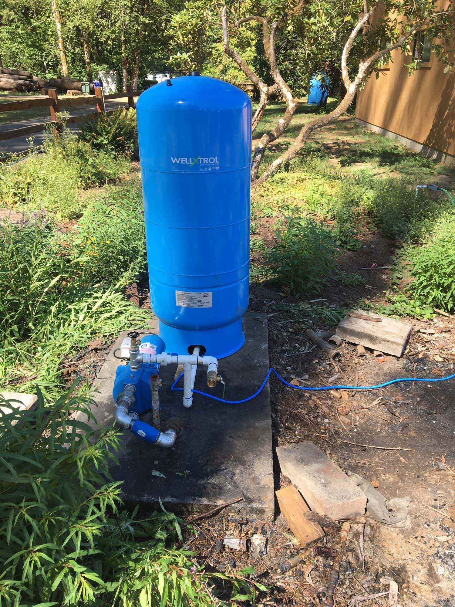 A blue water tank is sitting in the middle of a garden.