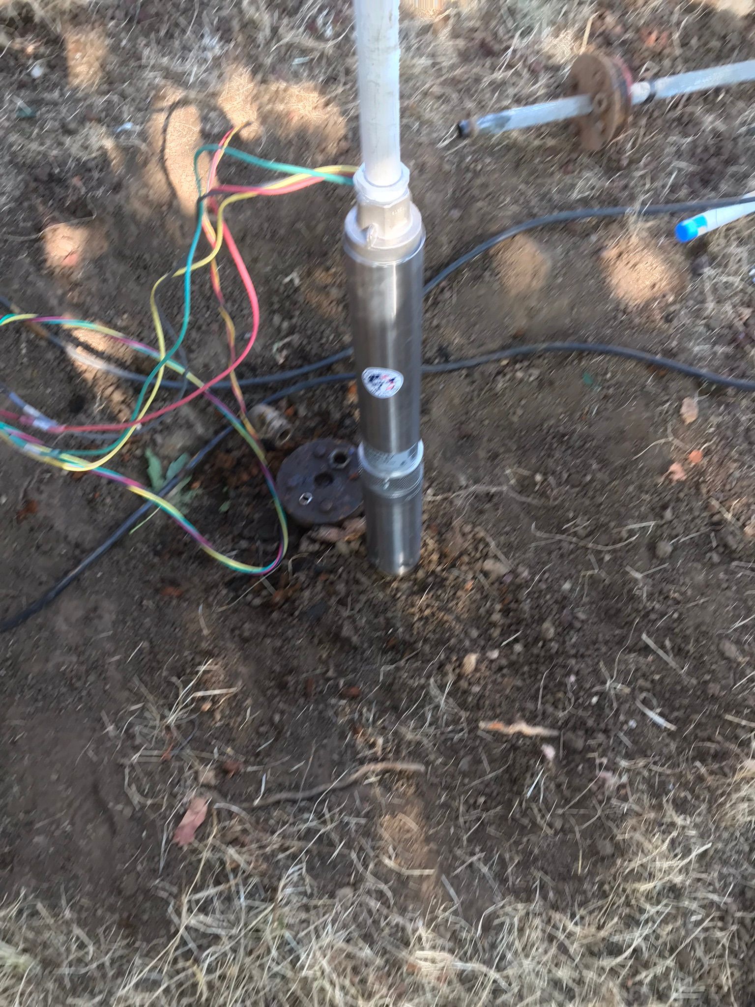 A water pump is sitting in the dirt next to a bunch of wires.