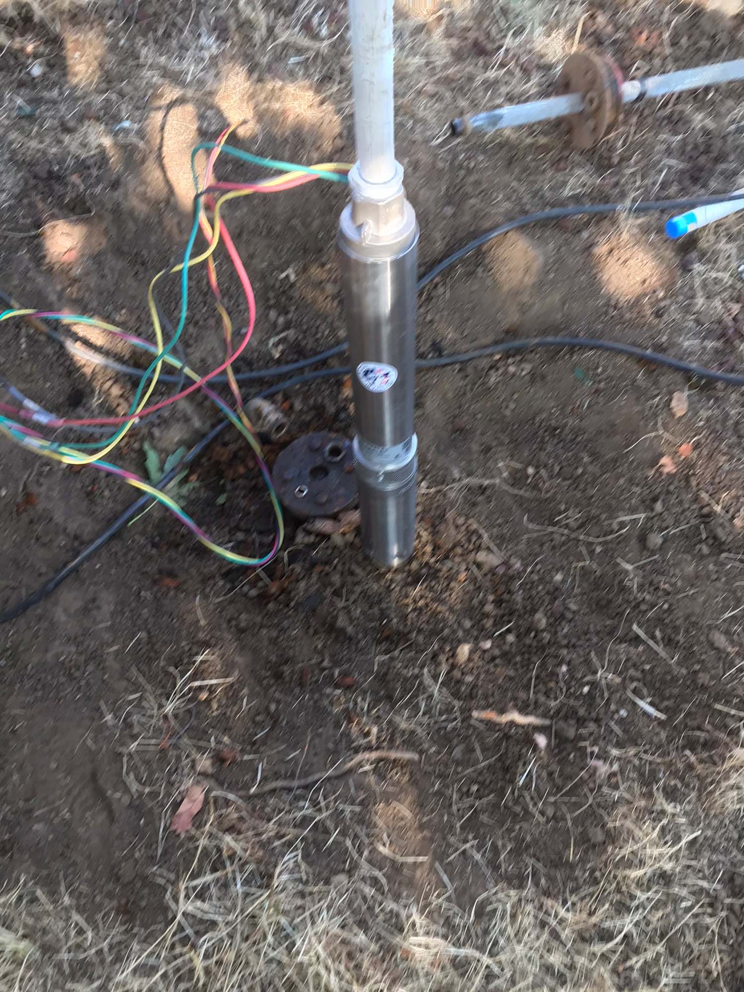 A water pump is sitting in the dirt next to a bunch of wires.
