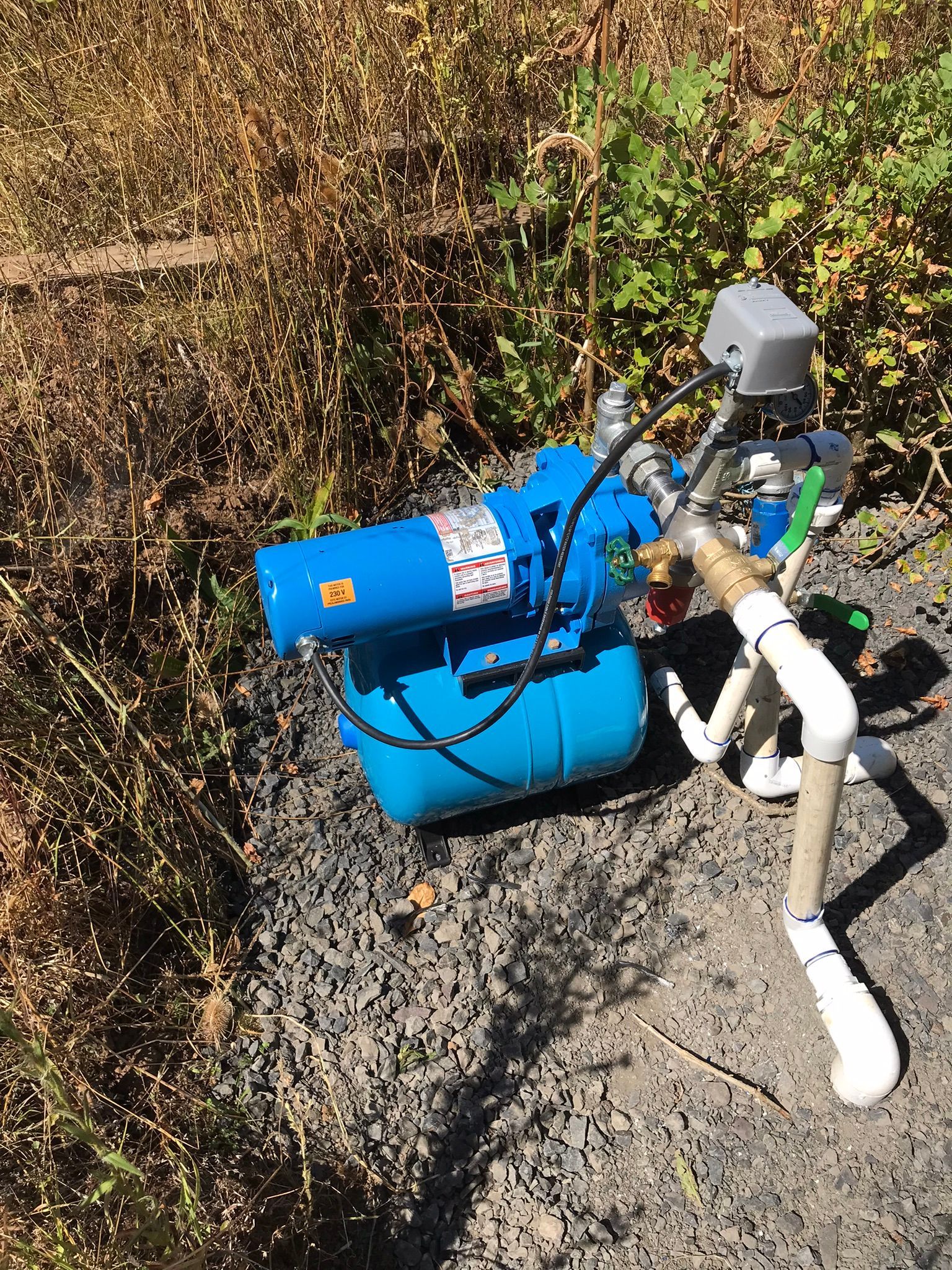 A blue water pump is sitting on the ground next to a pipe.