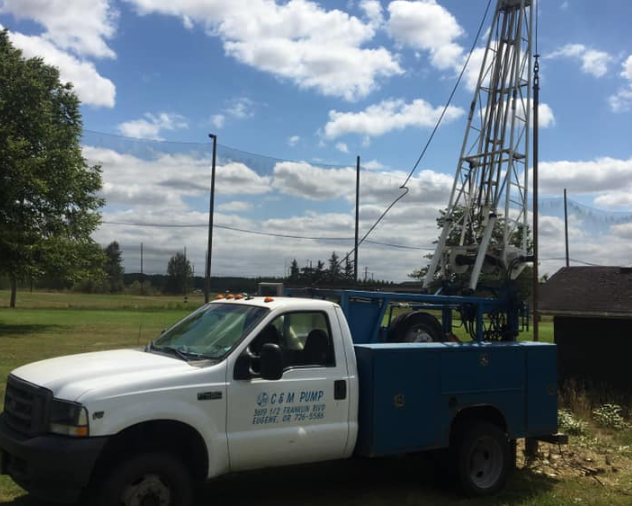 A white truck is parked in a field next to a drilling rig.