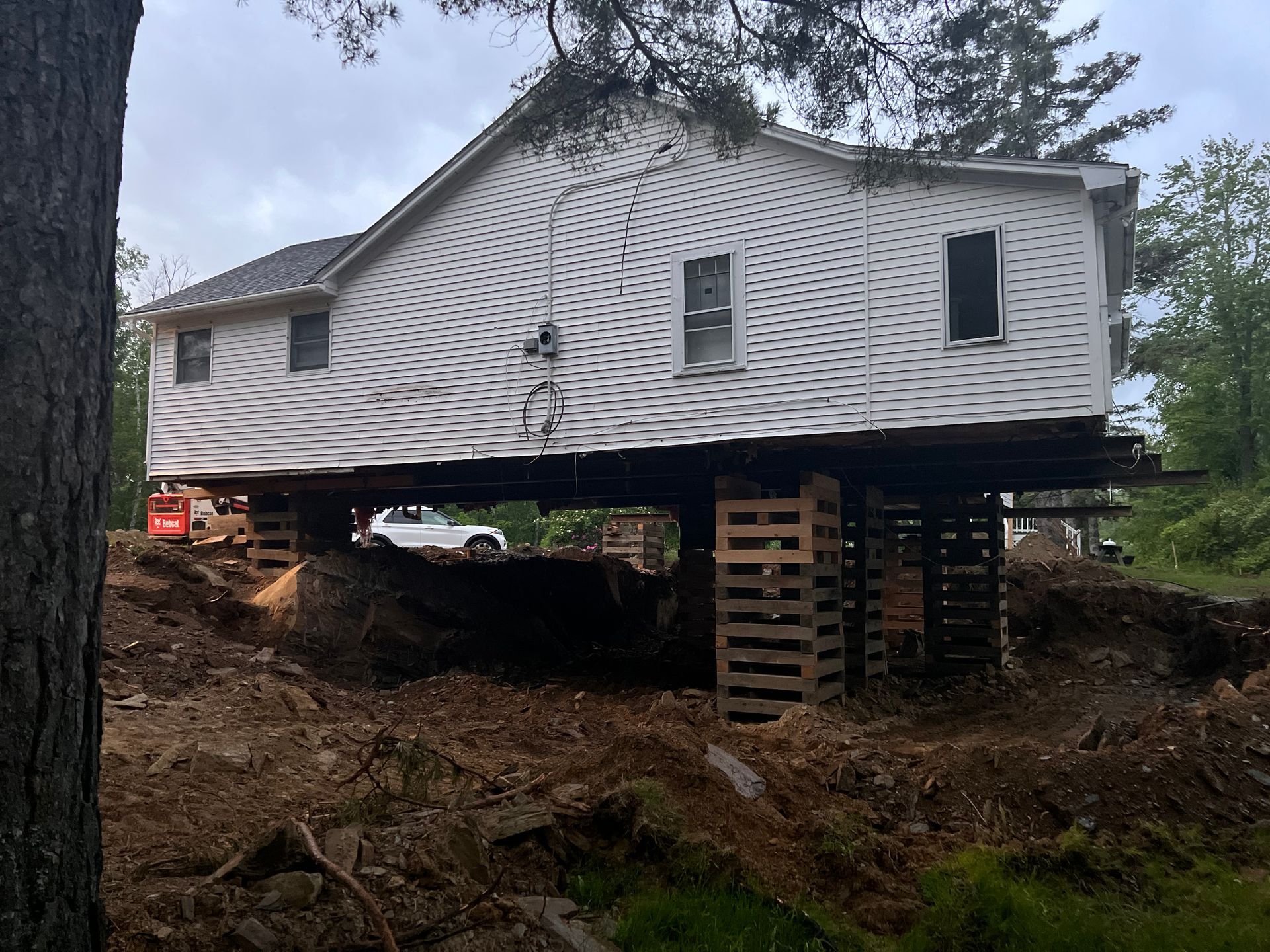 House raised on wooden supports during construction, with dirt surrounding it.