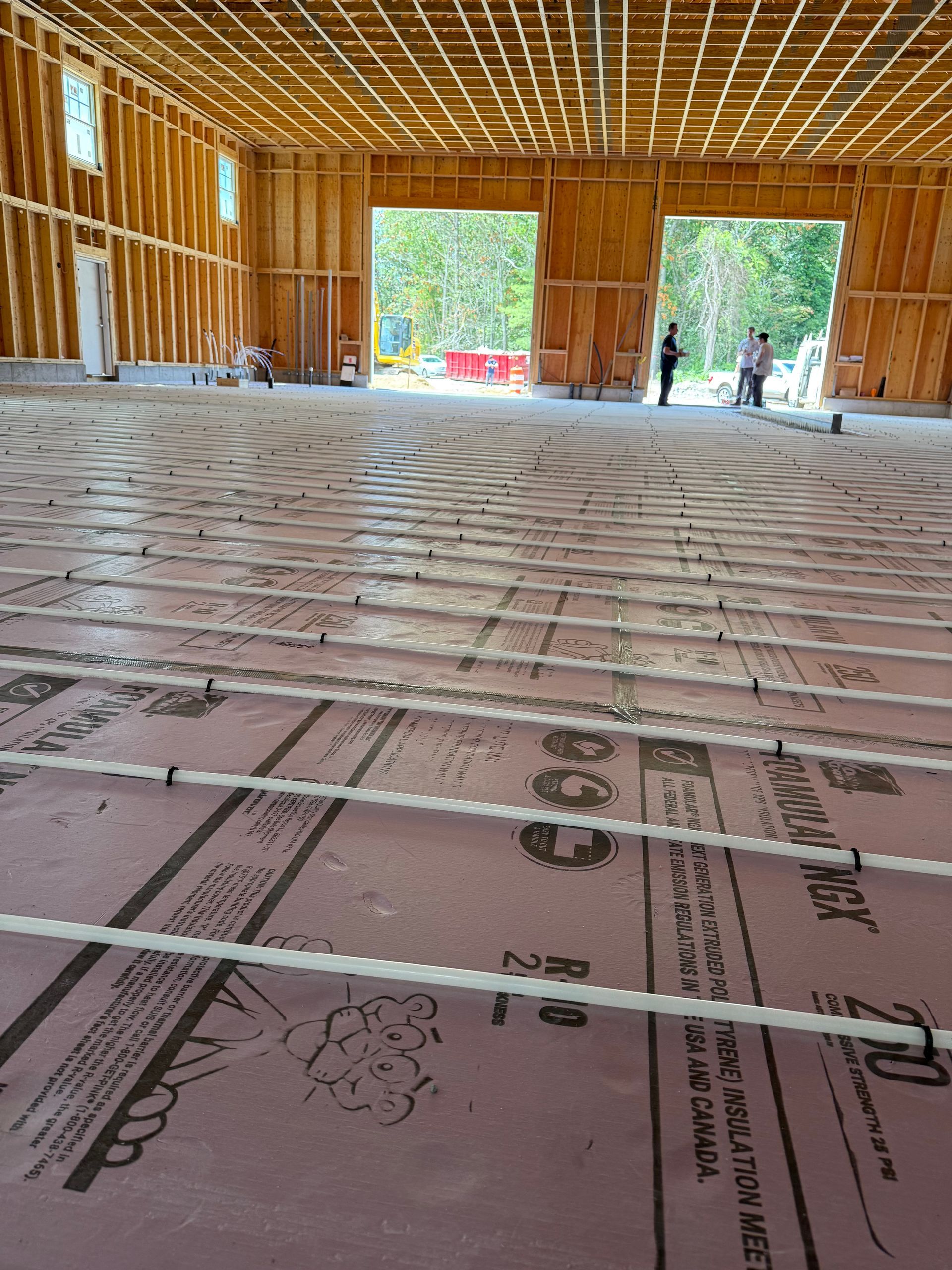 Interior of a building under construction. Pink insulation and white tubes cover the floor. Wooden frame walls and ceiling.