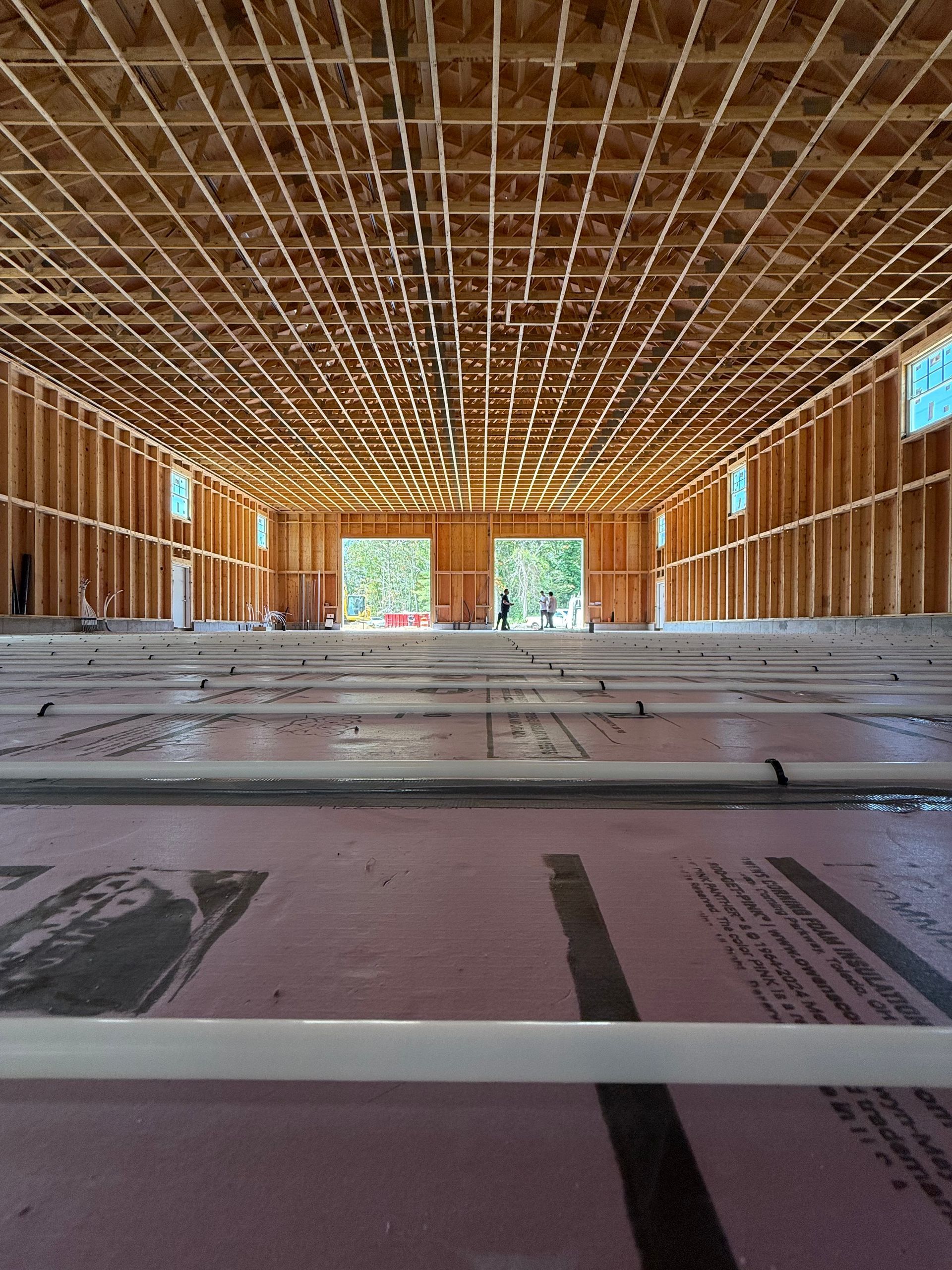 Interior view of a building under construction. Pink insulation covers the floor, wood framing on walls and ceiling.