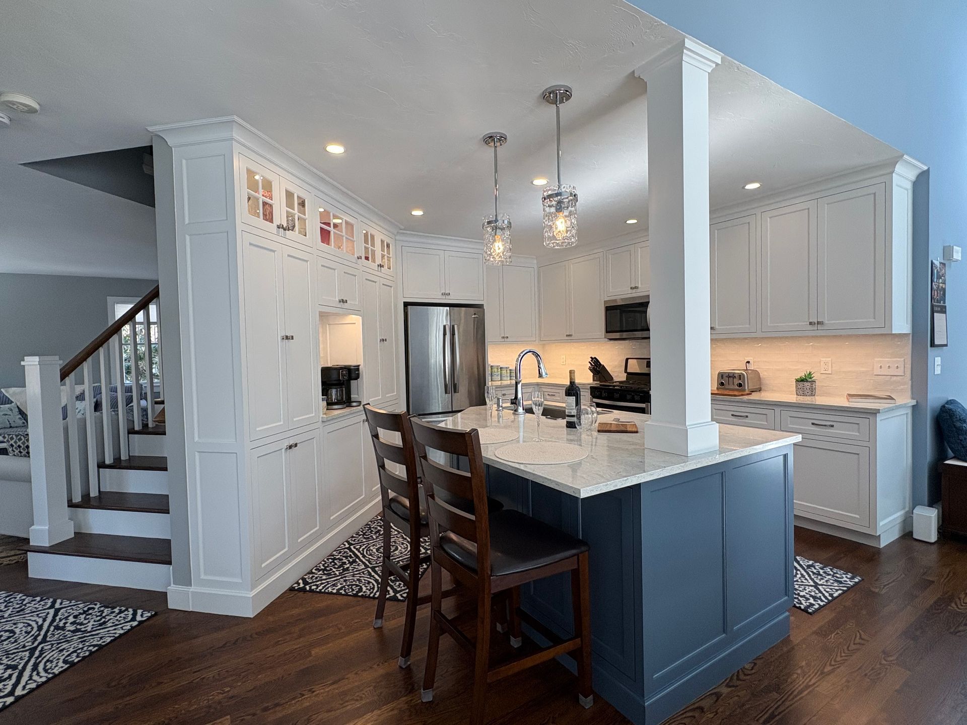 Kitchen with white cabinets, dark blue island, stainless steel appliances, and wood floors.