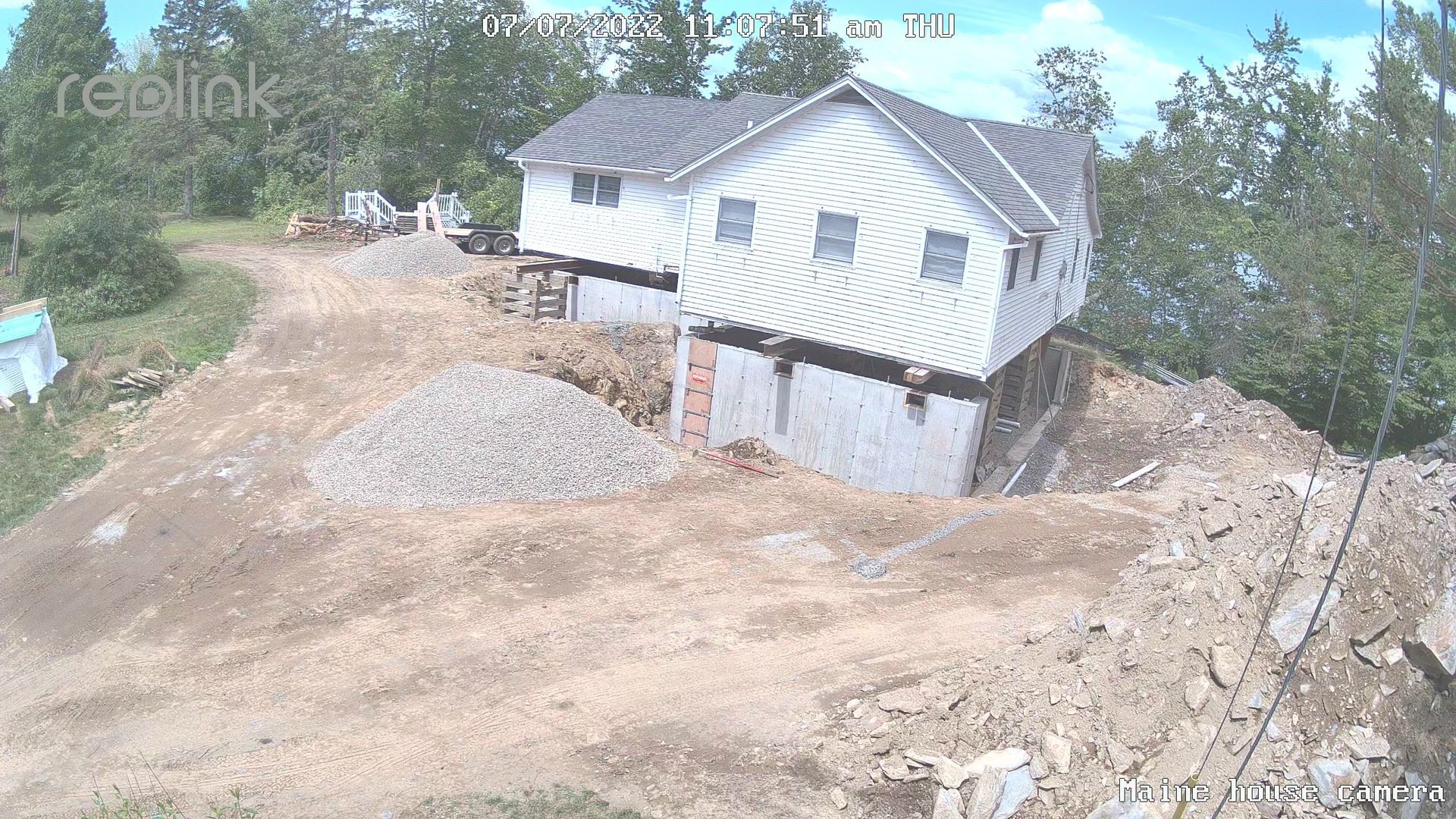 A white house sits on a hillside with excavation around its foundation. Piles of dirt and gravel surround the structure.