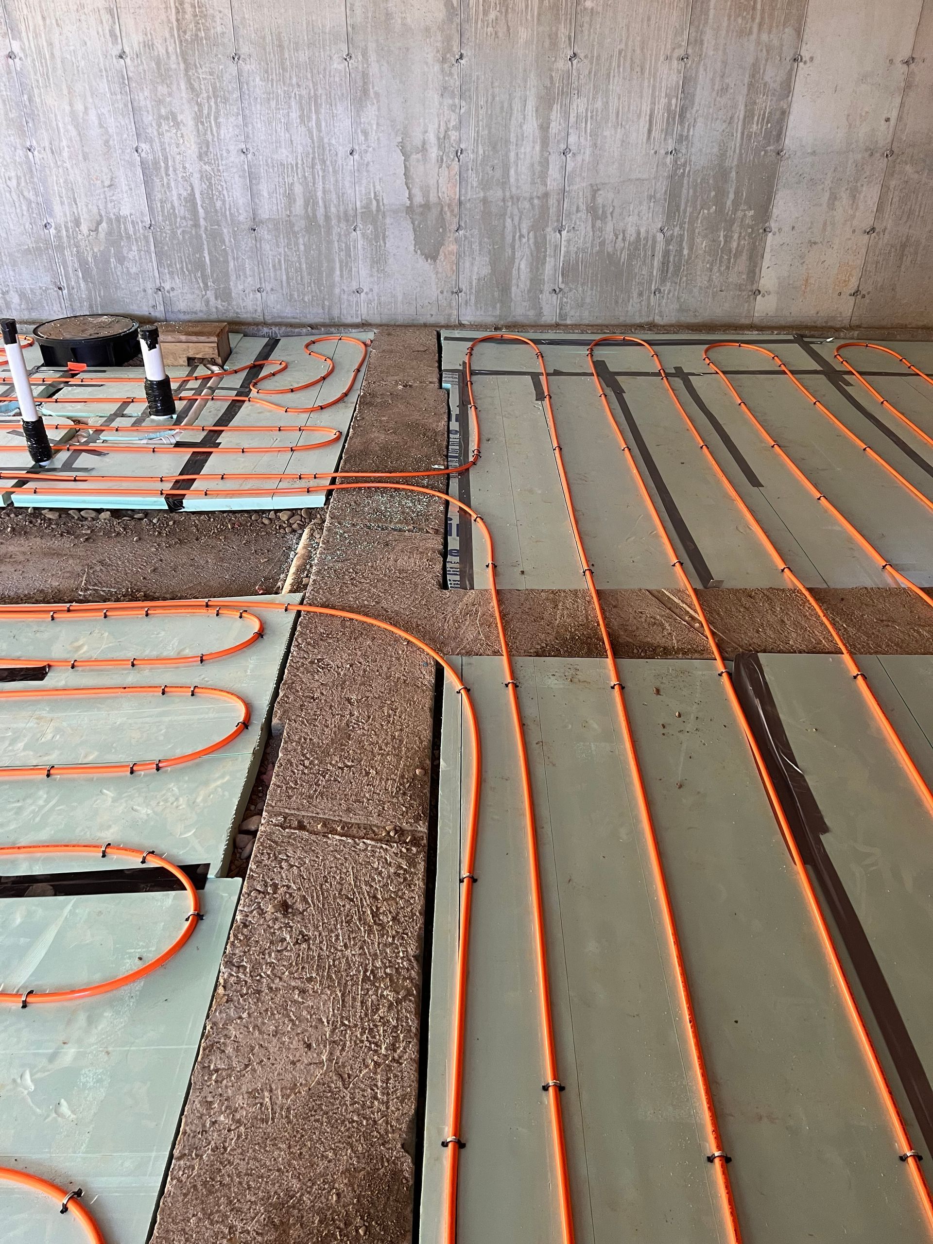 Orange radiant floor heating tubes laid on insulation boards, gravel and concrete wall.