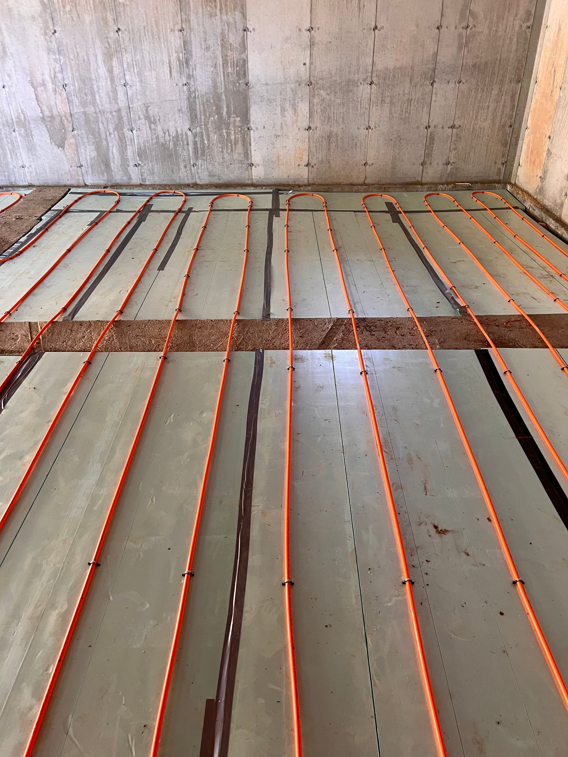 Orange radiant floor heating tubes installed on a floor, against a concrete wall.