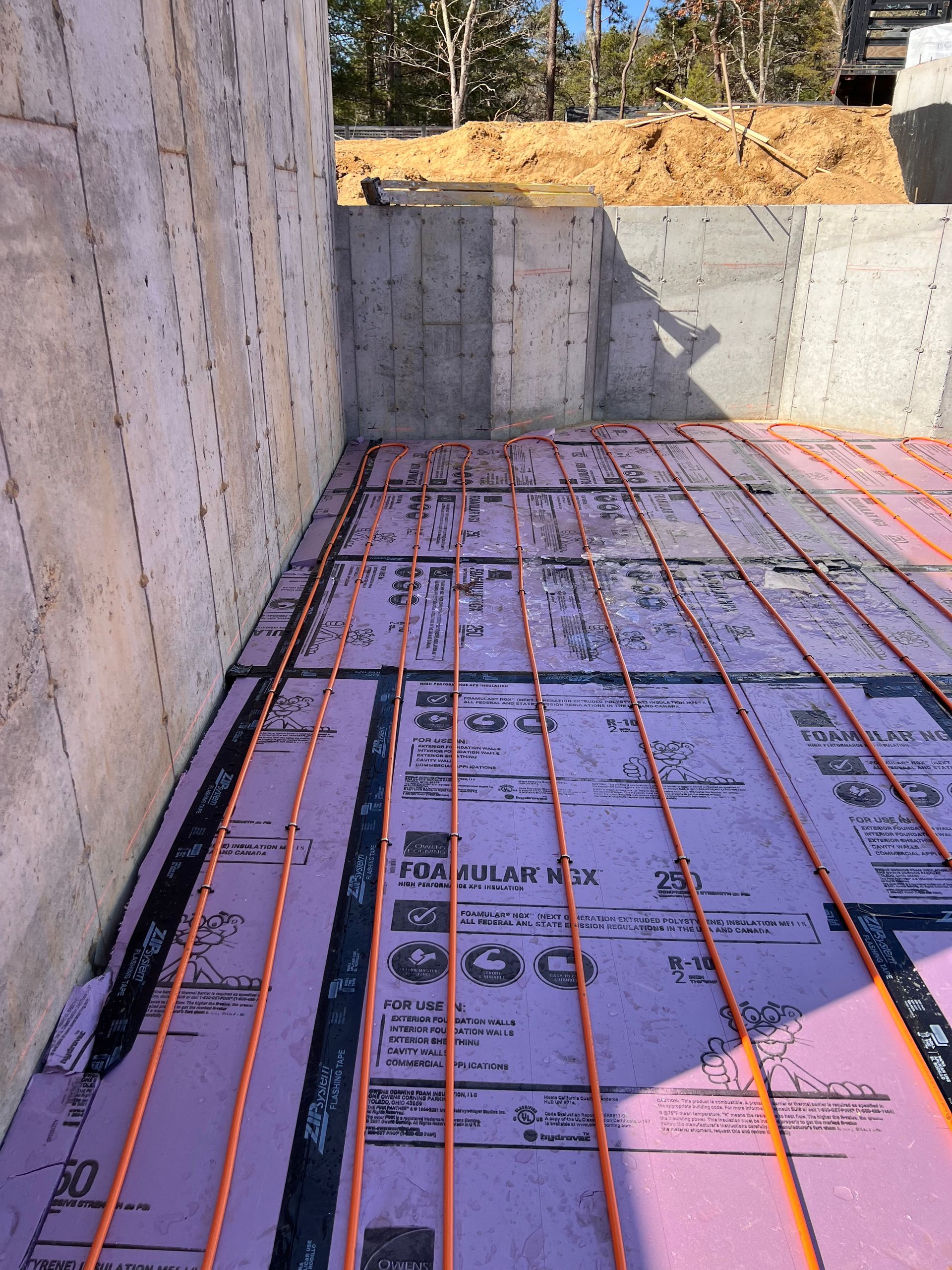Orange tubing laid on pink insulation within a concrete foundation, likely for radiant floor heating.