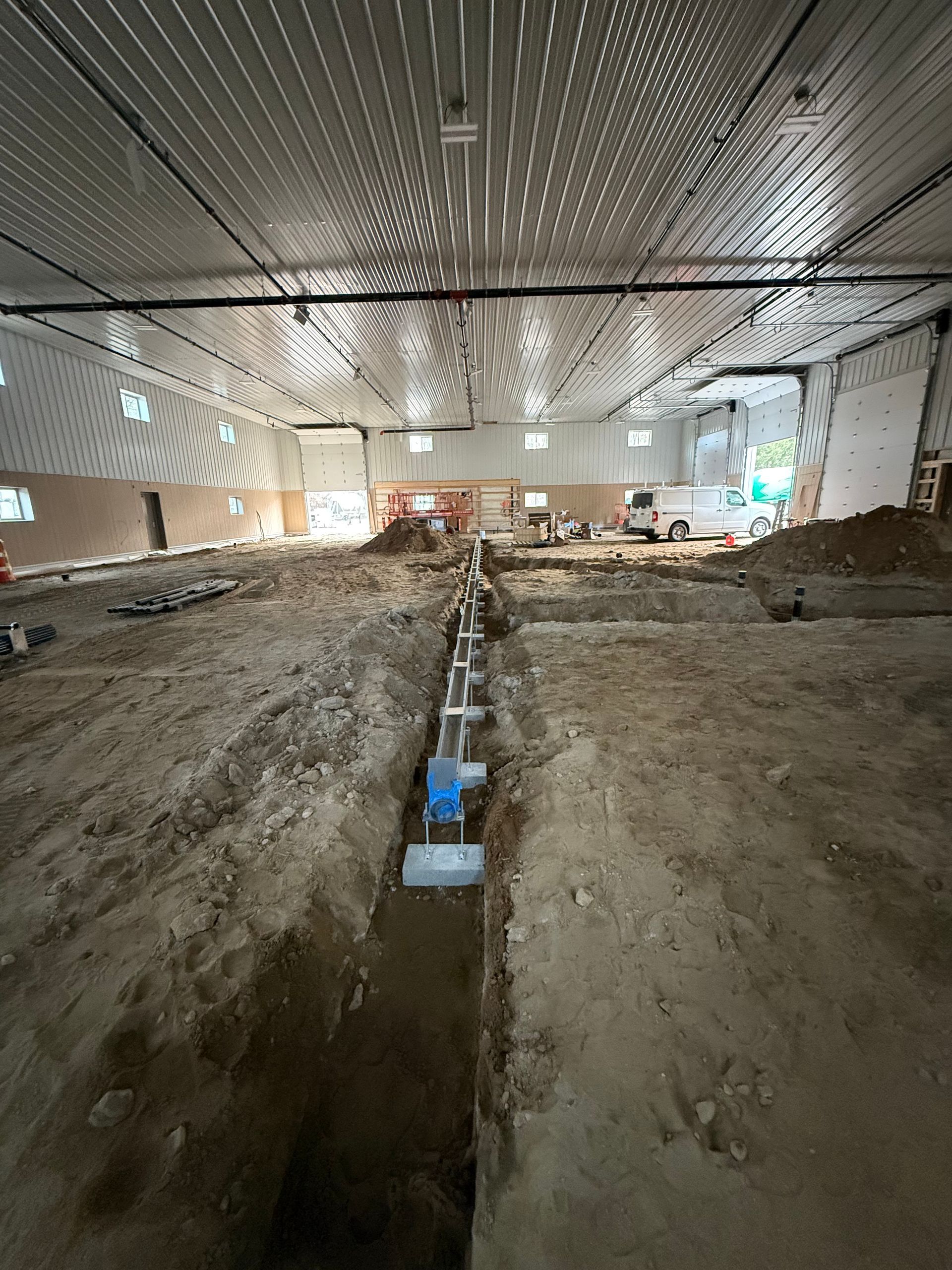 A long trench with pipes running through it inside a large building under construction.