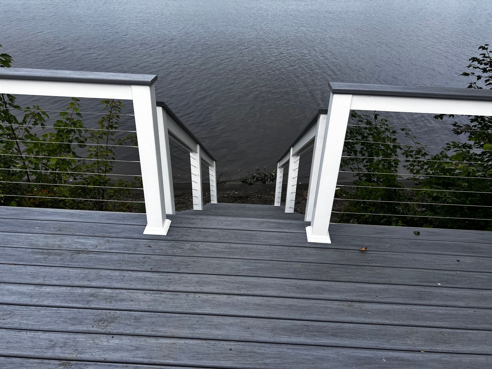 Staircase leading down to water, white railings, gray decking, overcast sky.