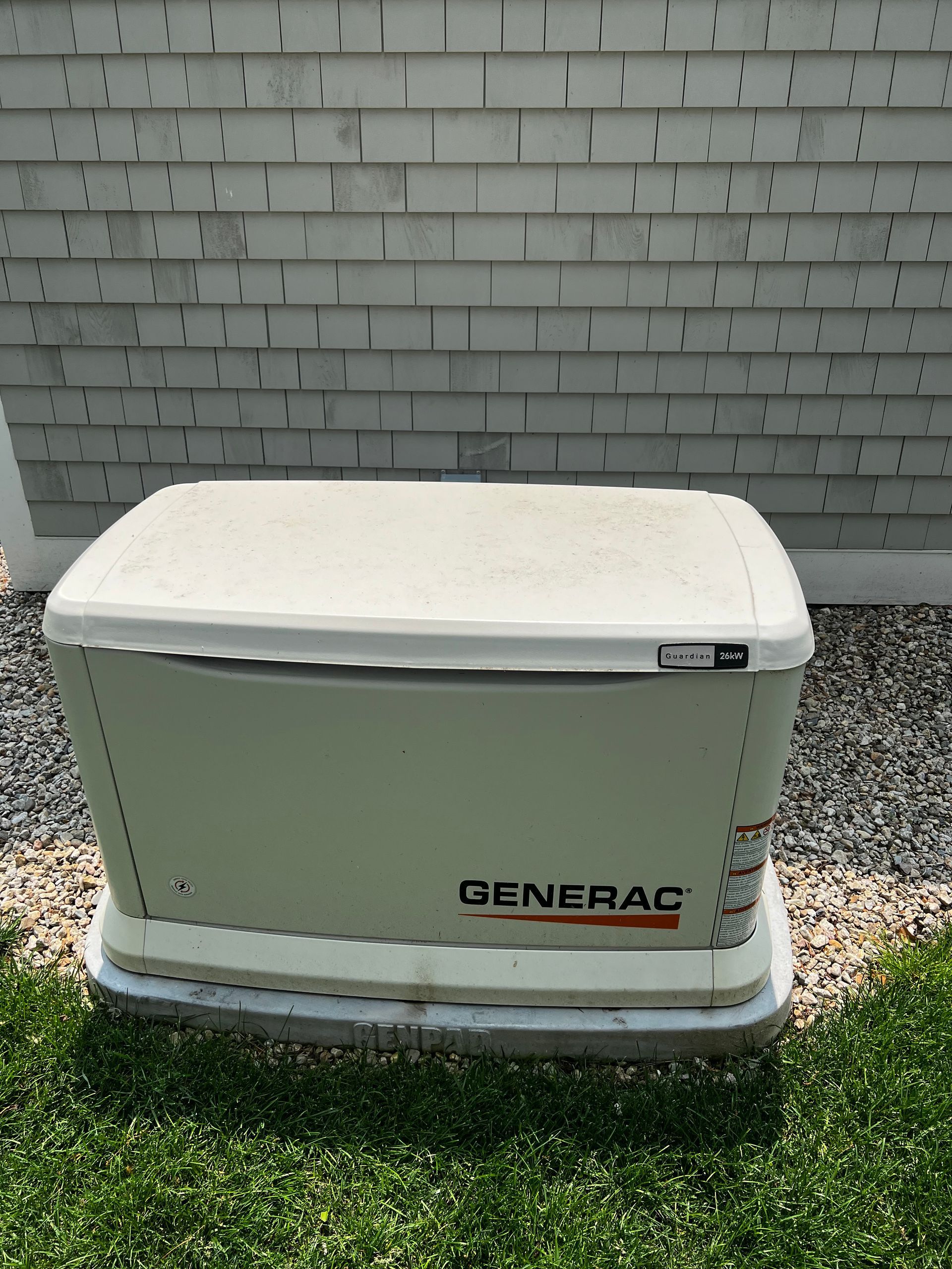 Generac standby generator on a concrete pad, next to a shingled building wall.