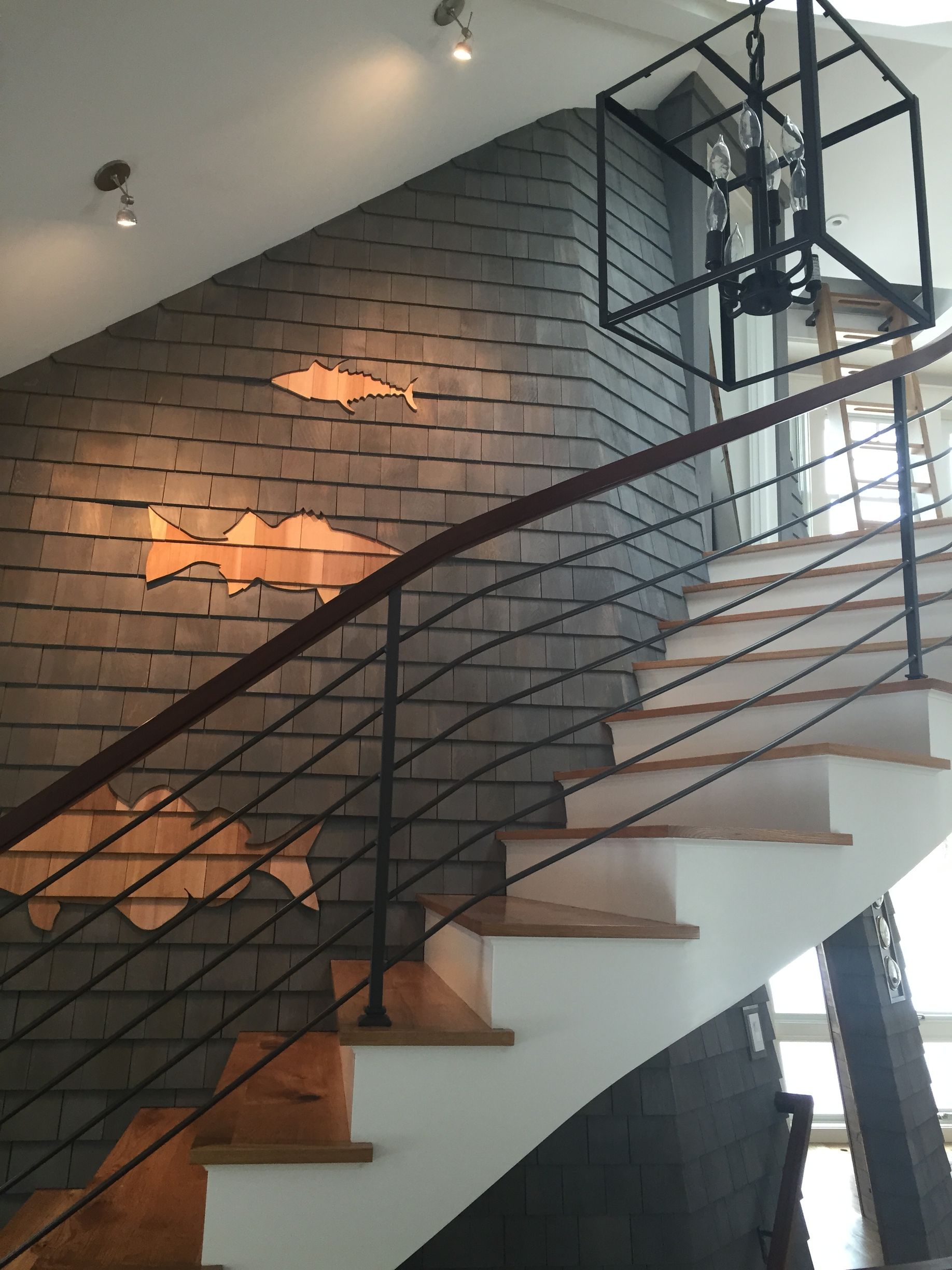 Staircase with wooden steps and metal railing; slate wall with fish cutouts; black cage light fixture.