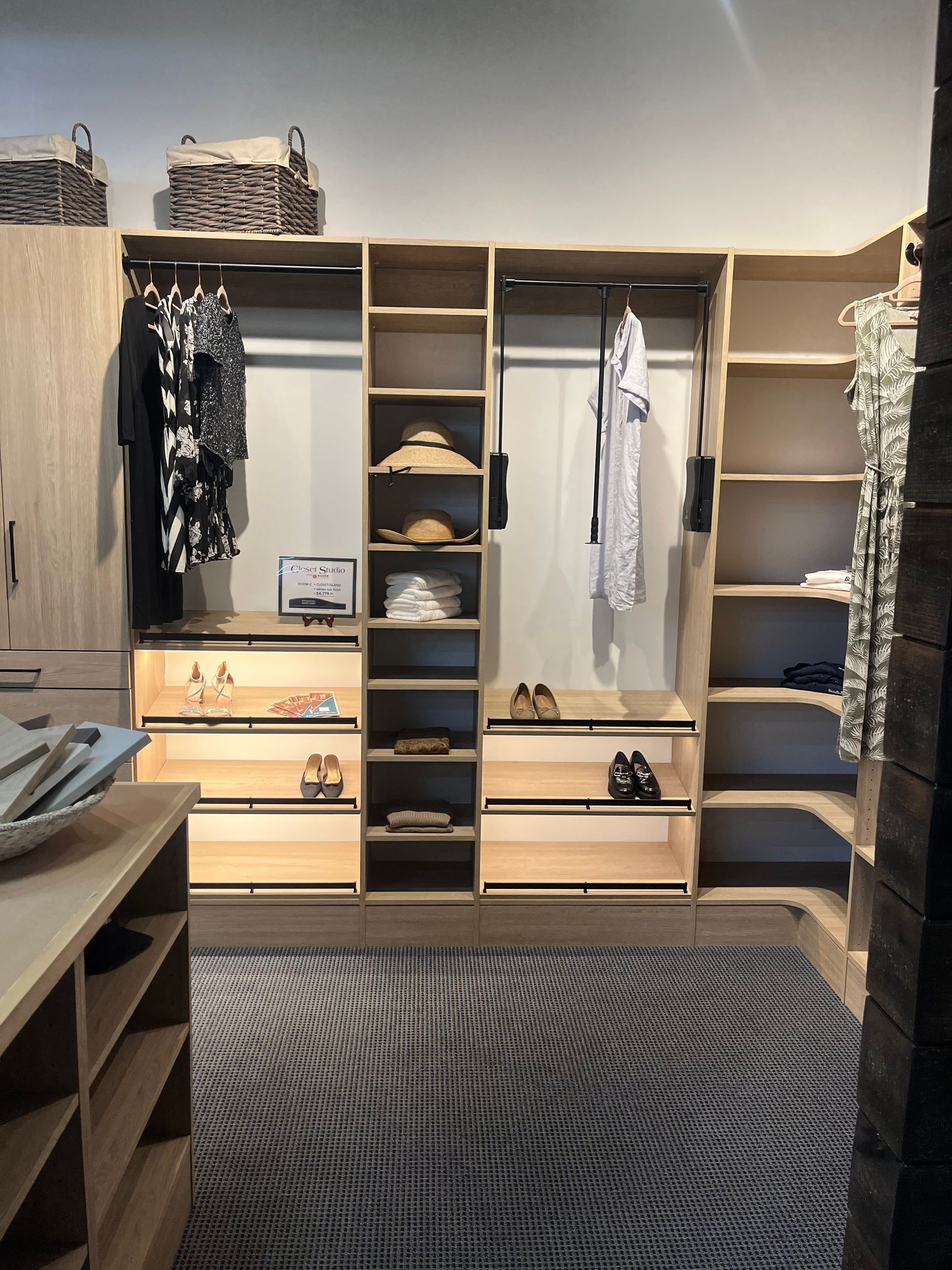 Wooden walk-in closet with hanging clothes, shelves, drawers, and a patterned rug.