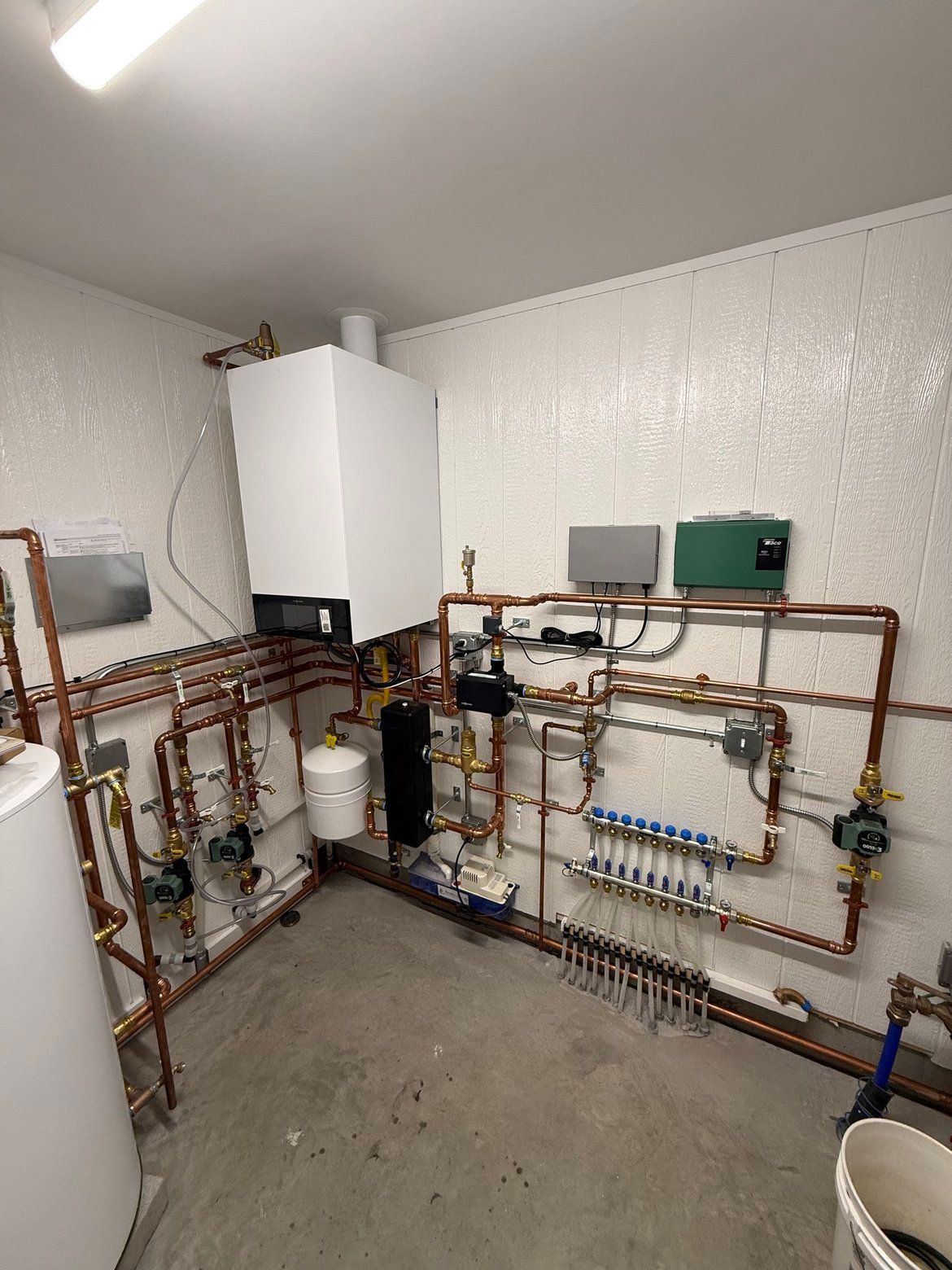 Heating system with white boiler, copper pipes, and other equipment in a utility room.