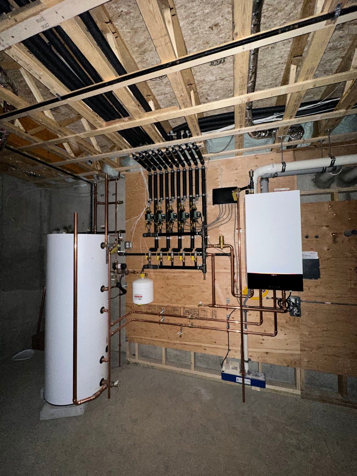 Basement with heating system components, including a water heater, boiler, and pipes.