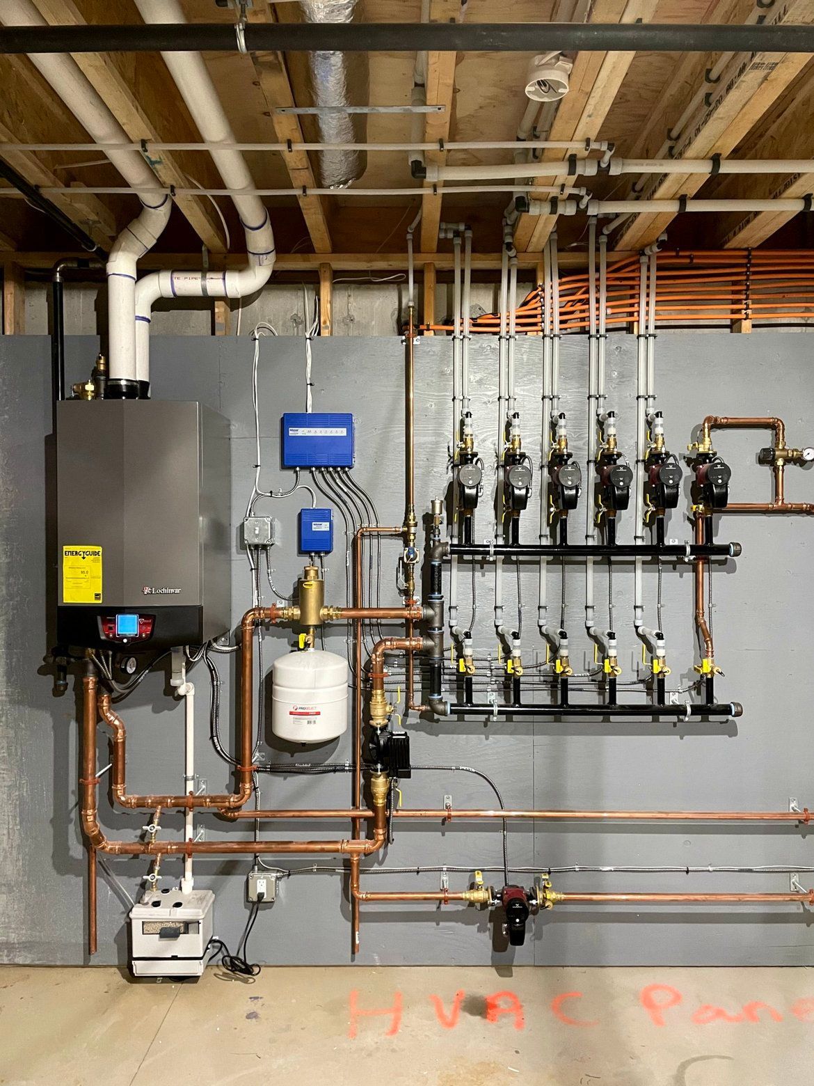 Copper pipes and heating system components mounted on a gray wall, including a boiler and distribution manifold.