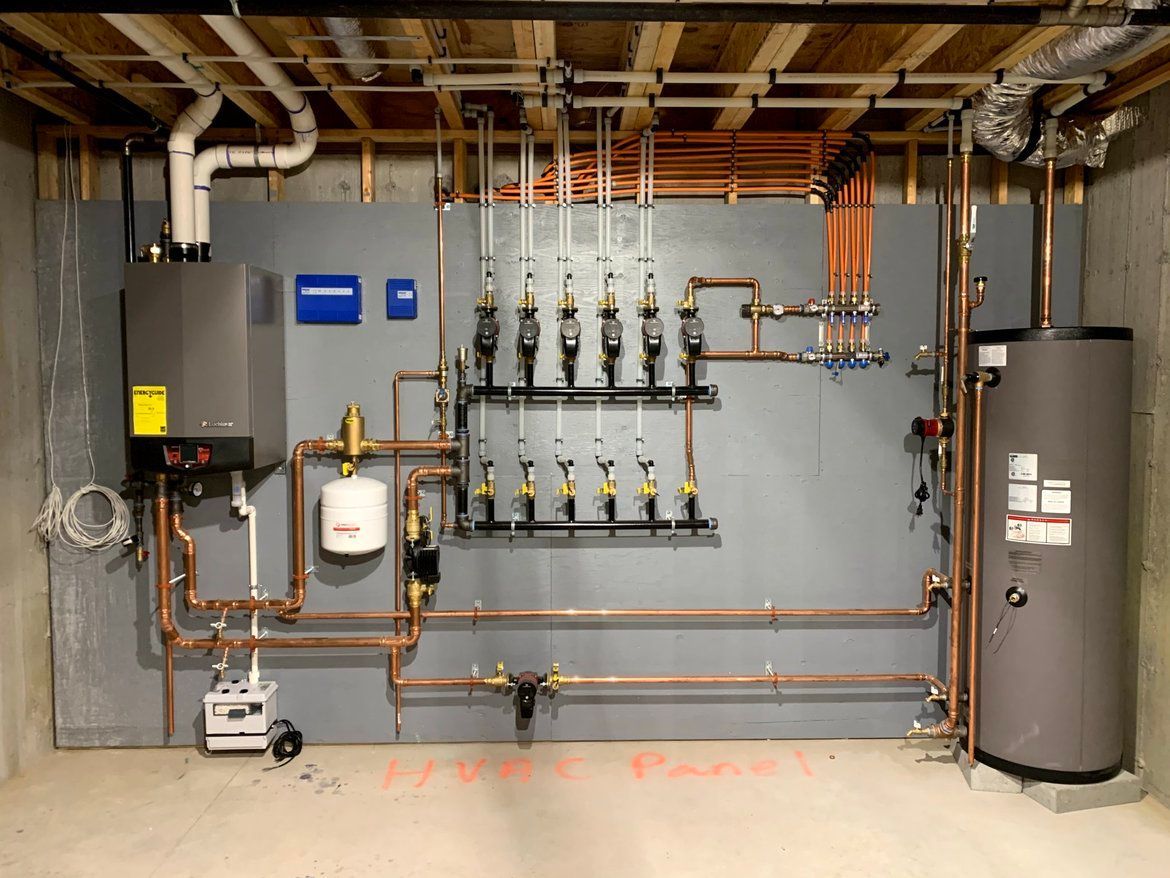 Copper pipes and plumbing equipment on a gray wall in a mechanical room, including a water heater and boiler.