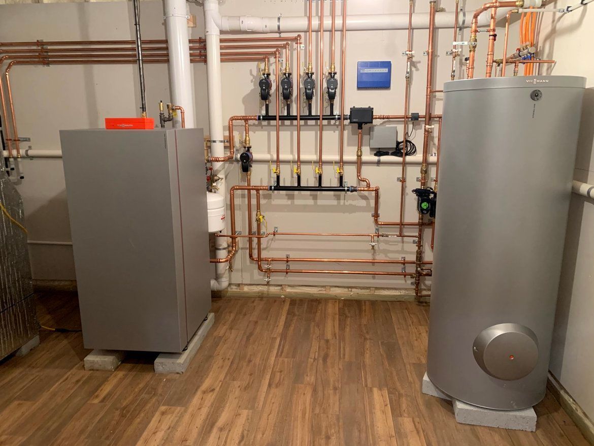 Heating system with copper pipes and gray tanks in a basement.