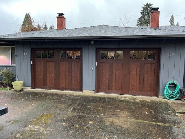 A house with two wooden garage doors and a green hose in front of it.