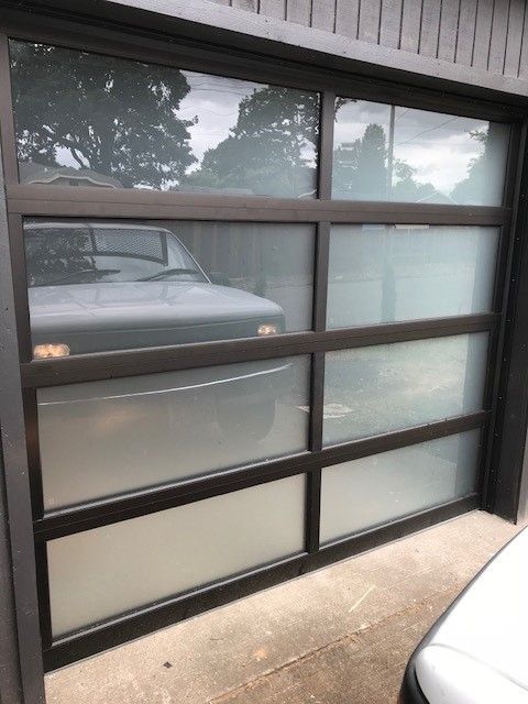 A car is parked in front of a garage door with a lot of windows.