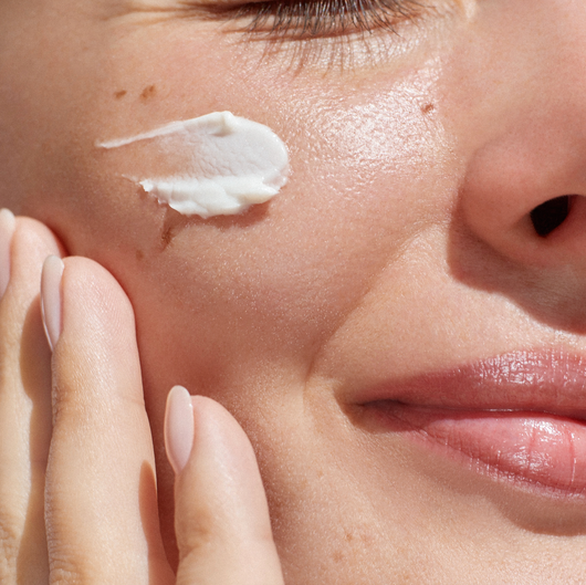 A woman is applying cream to her face.