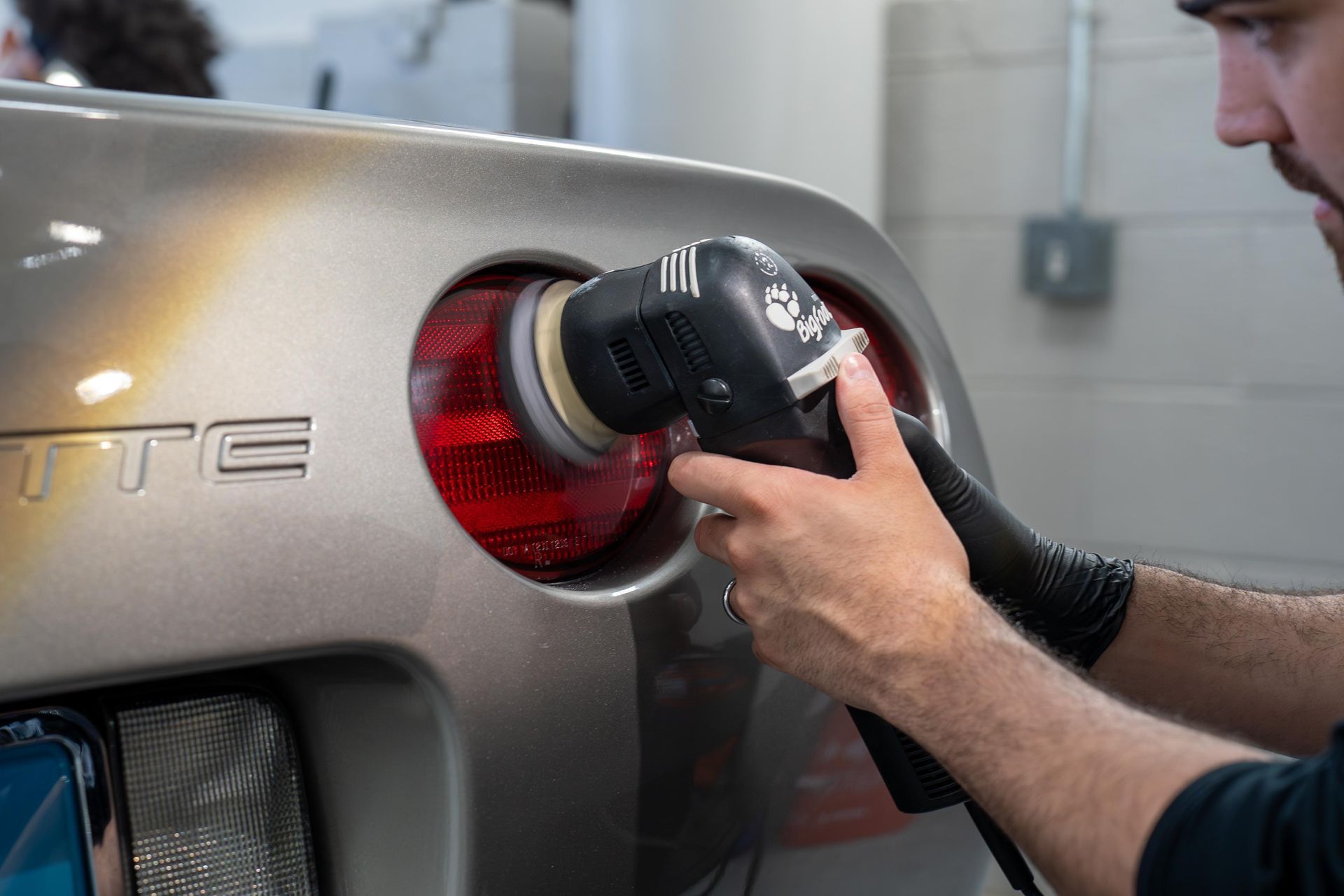 Man polishing a car's taillight with a buffer, outdoors.