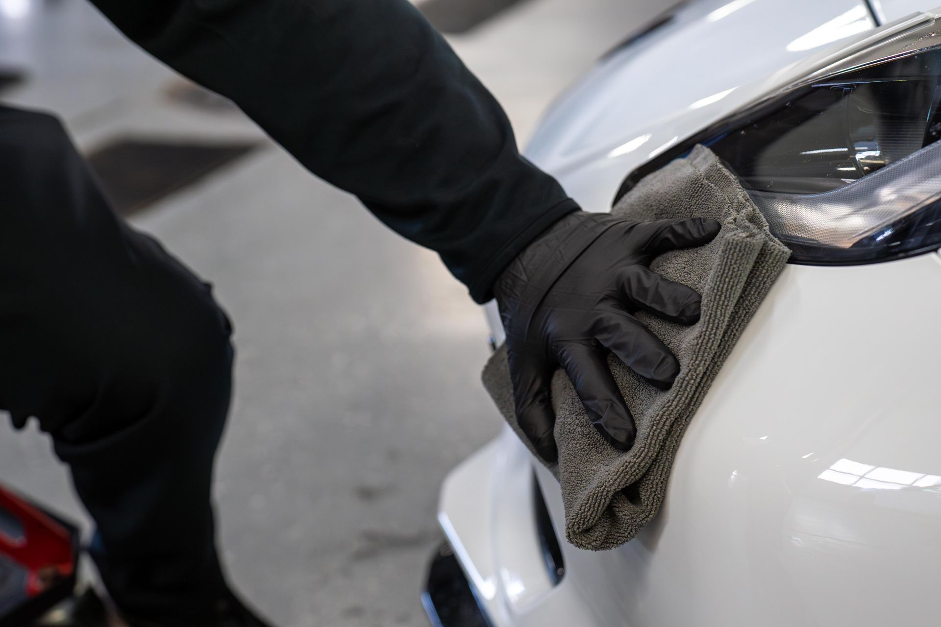 A person wearing black gloves is cleaning a white car with a towel.