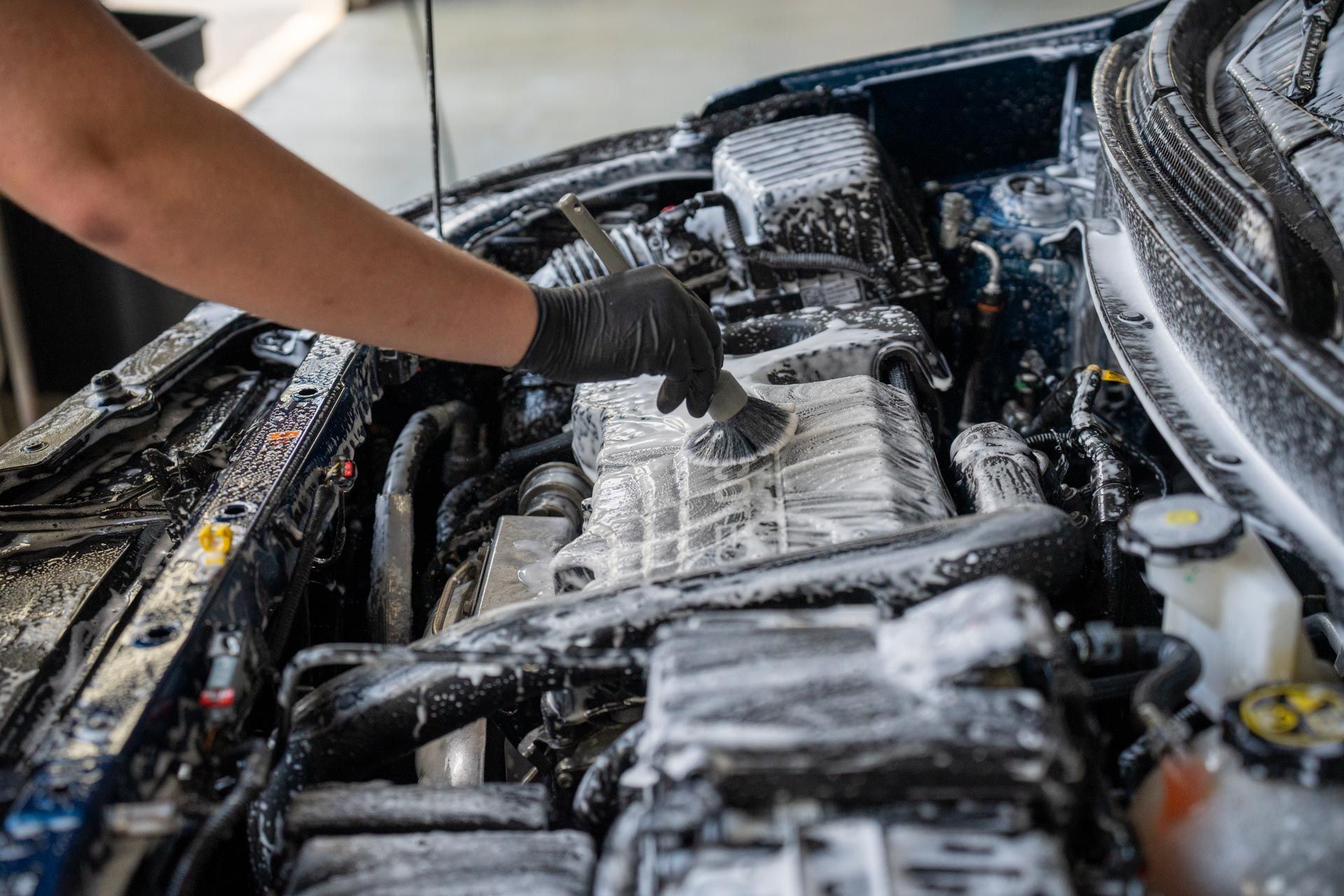 A person is cleaning the engine of a car with a brush.