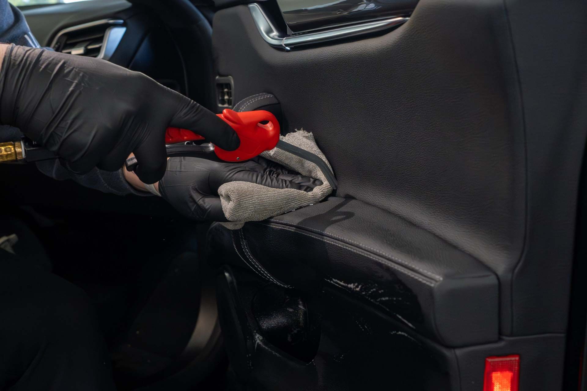 A person wearing black gloves is cleaning a car door with a towel.