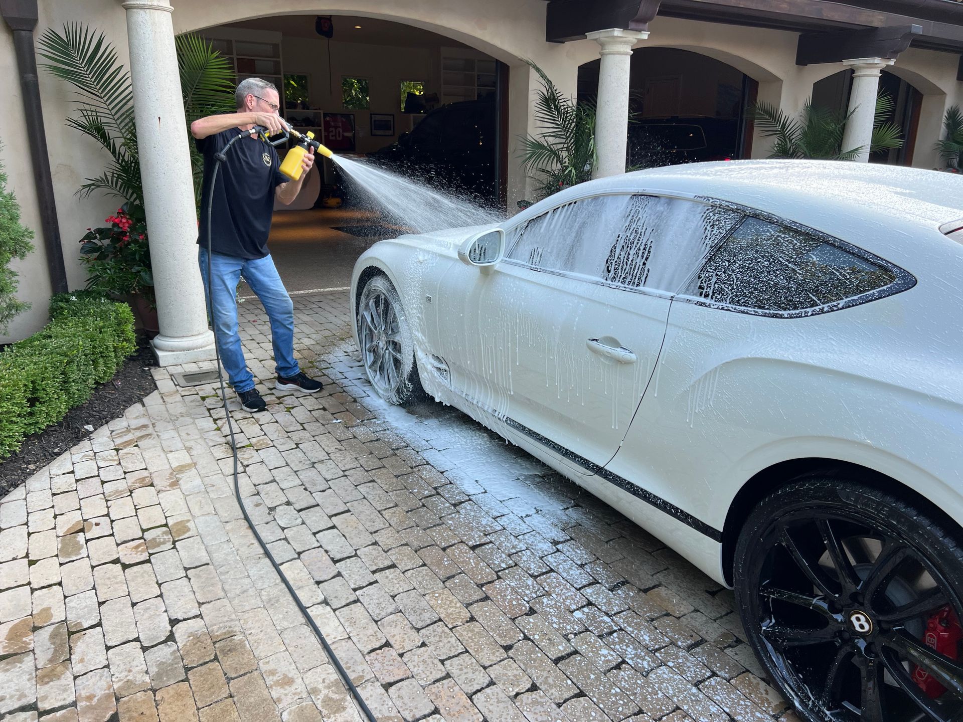 Man washing a white car with foamy soap in a driveway.
