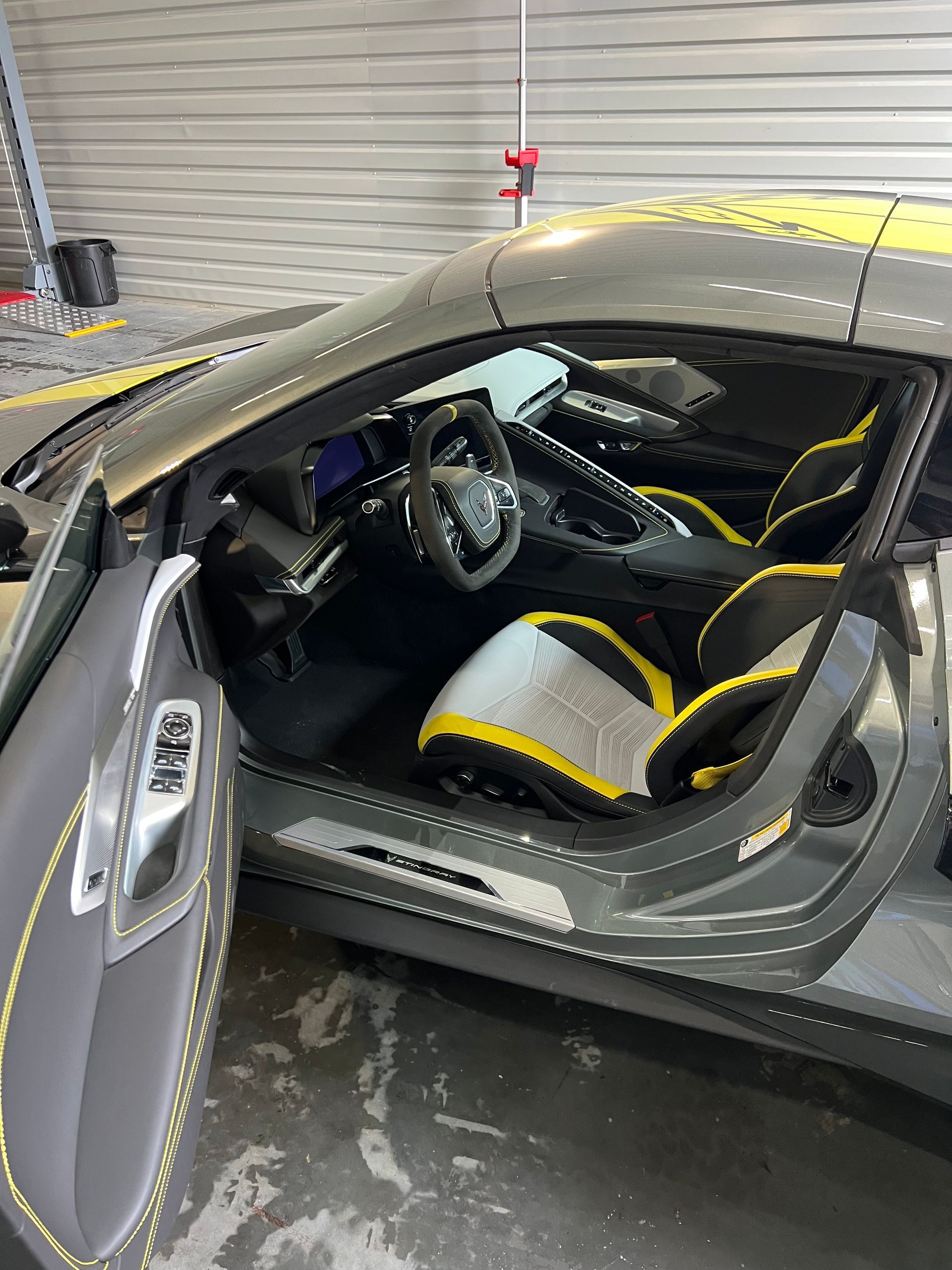 Gray sports car interior with yellow accents. Door open, seats and dashboard visible.