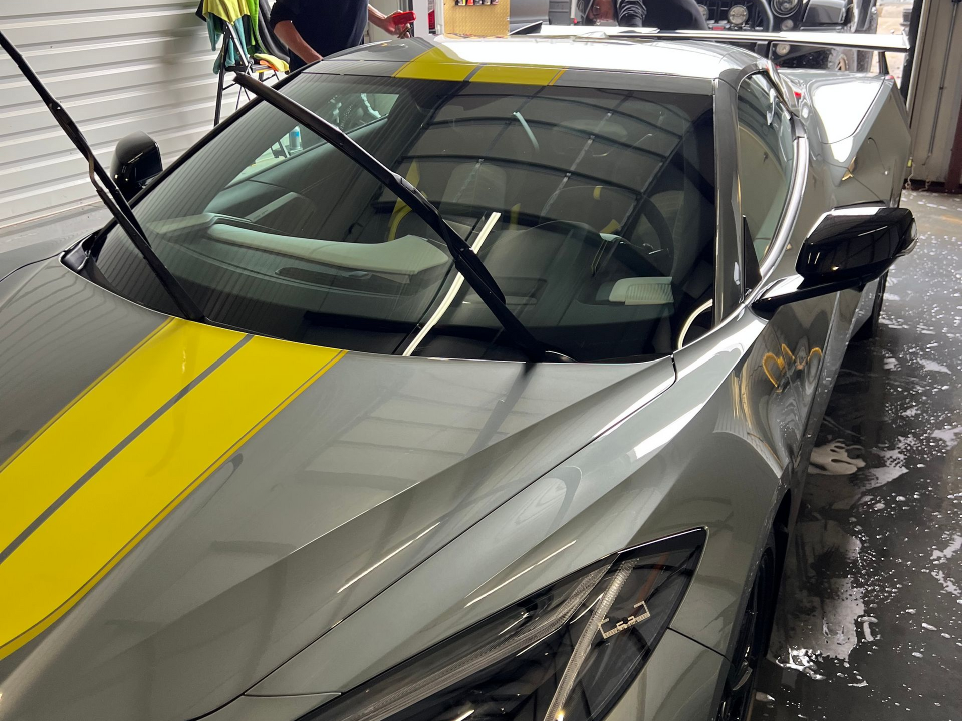 Gray sports car with yellow stripes being cleaned; wipers up.