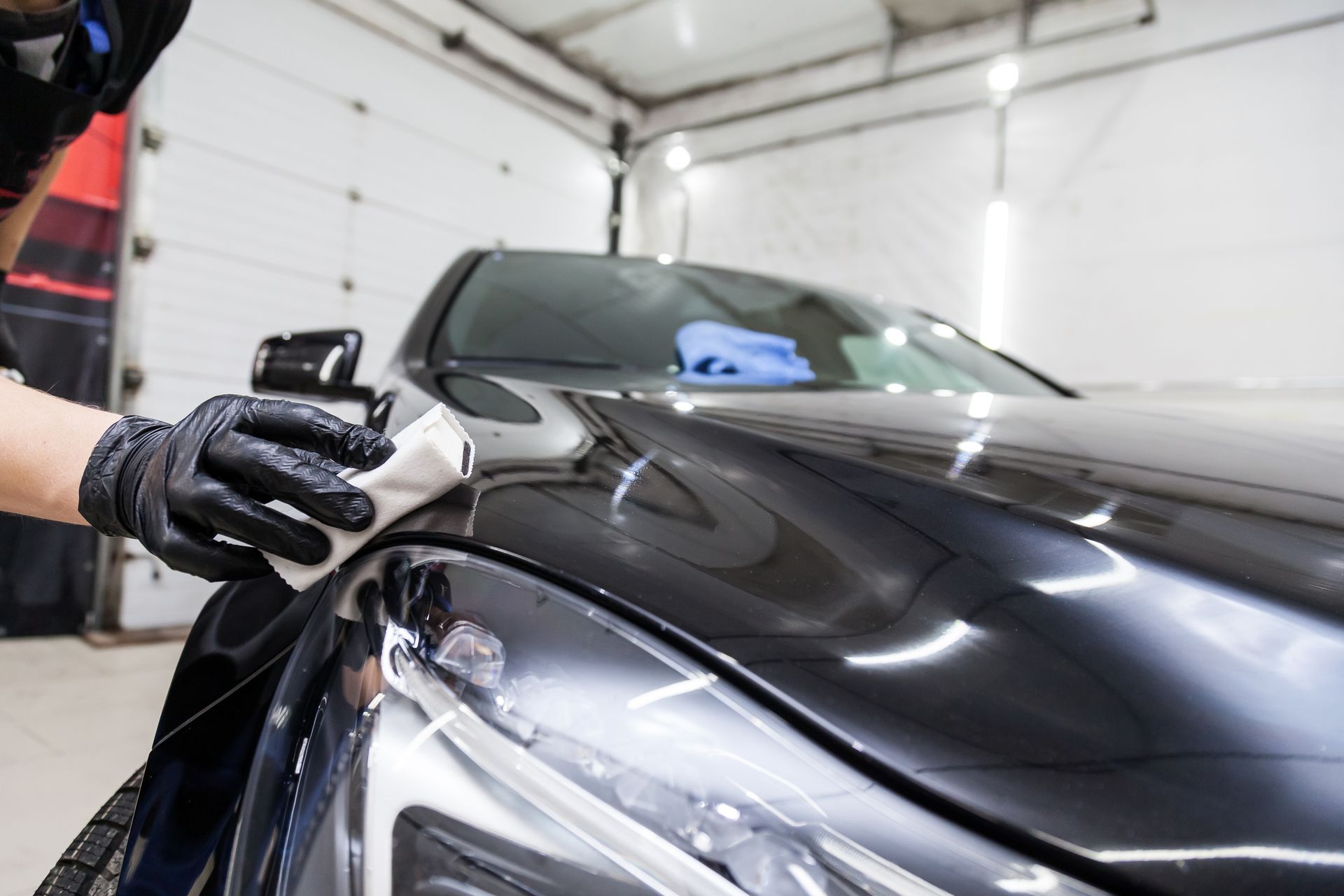 A man is polishing the hood of a black car in a garage.