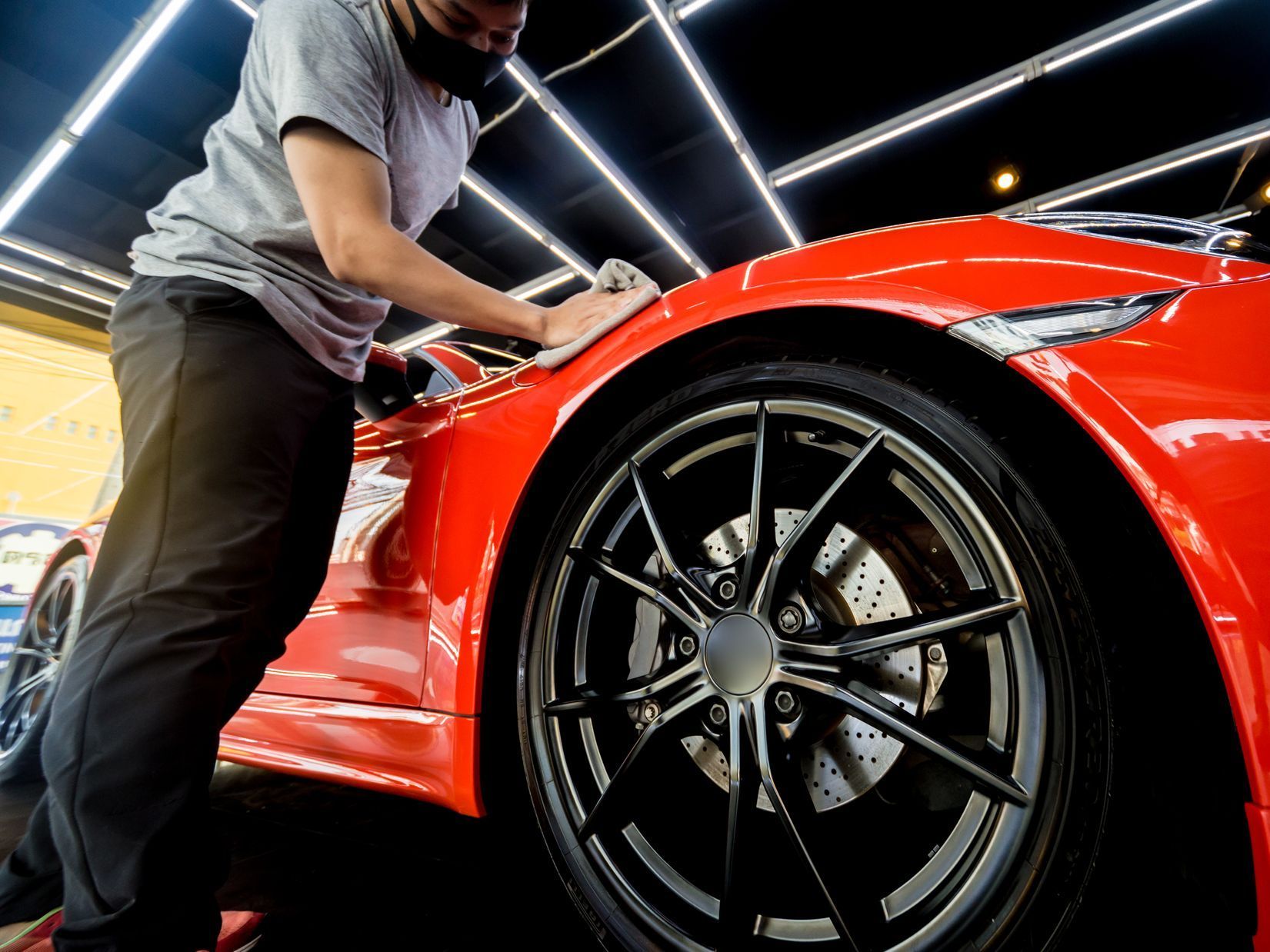 Person wearing a mask cleaning a red sports car.