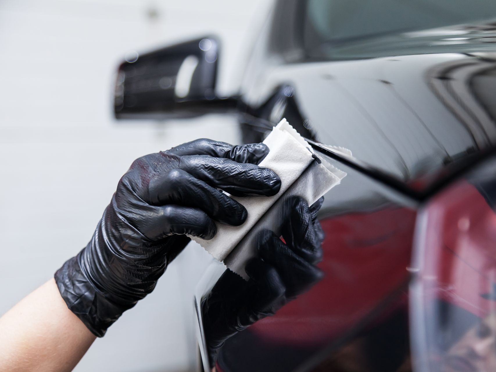 A person wearing black gloves is polishing a black car with a sponge.