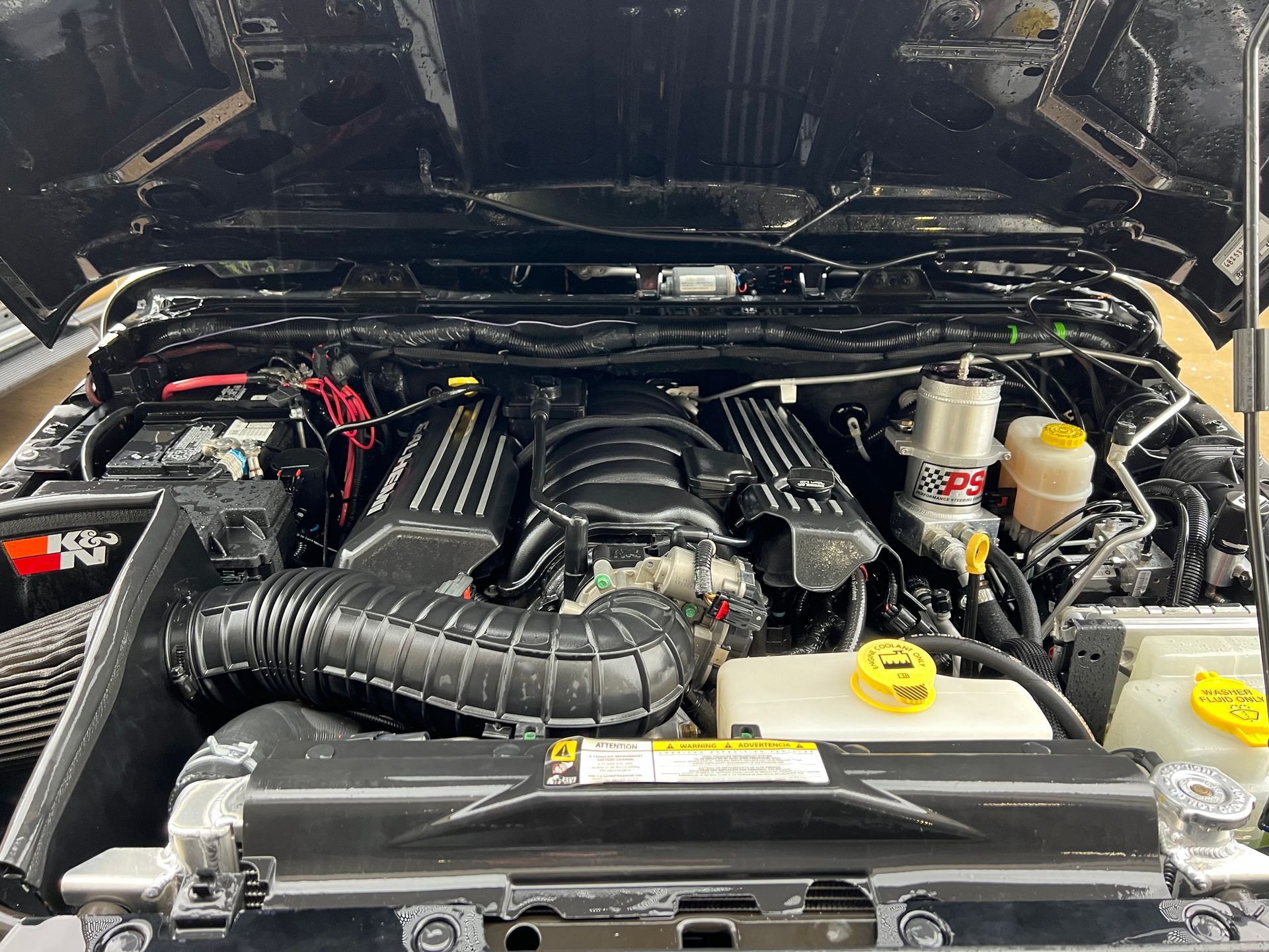 Black engine bay of a Jeep Wrangler, revealing a custom engine and air intake system.