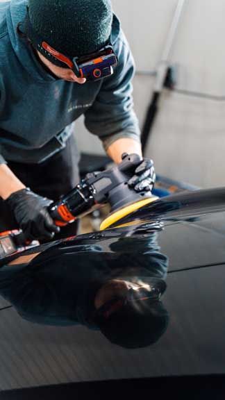 A man is polishing a black car with a machine.