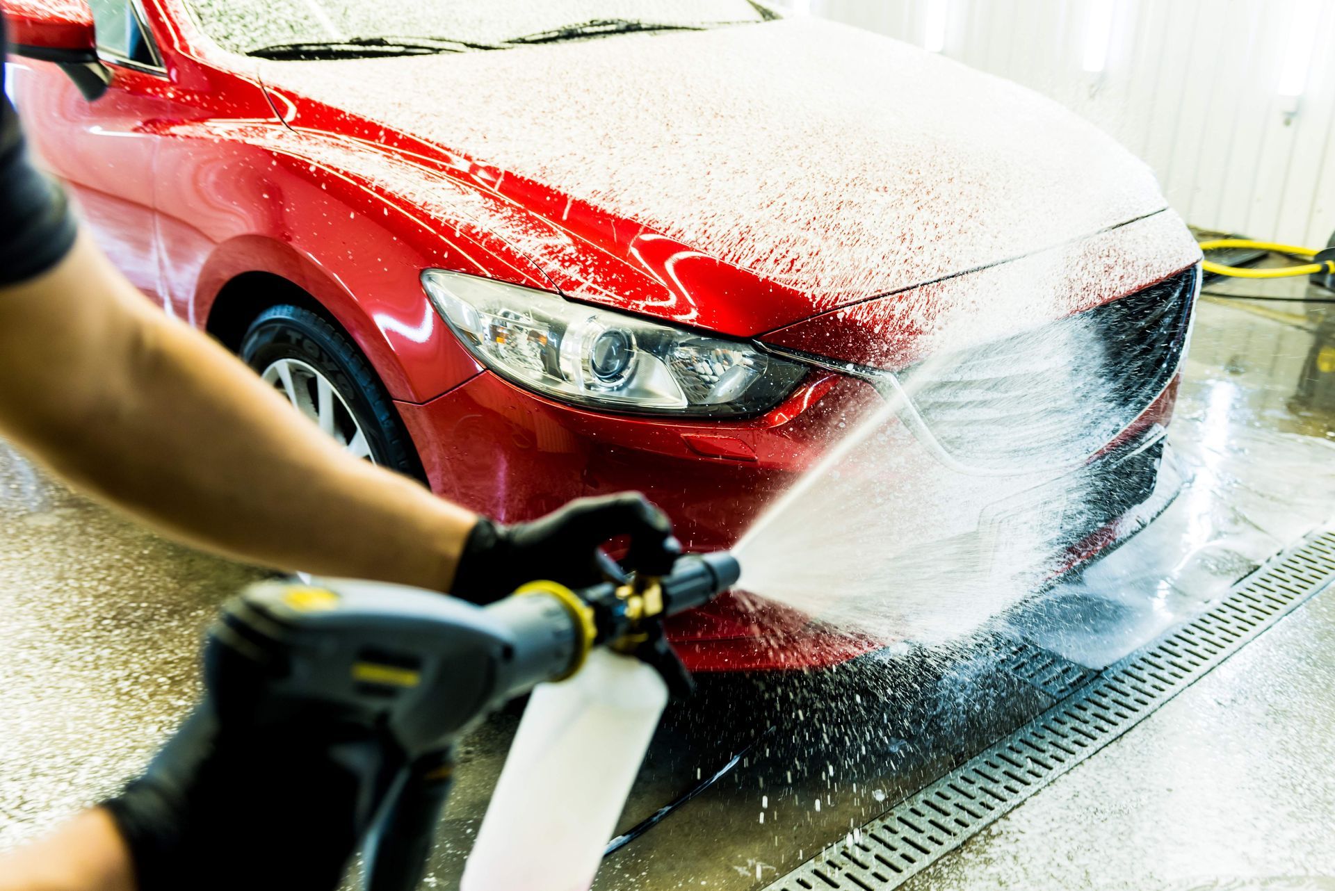 A person is washing a red car with a high pressure washer.