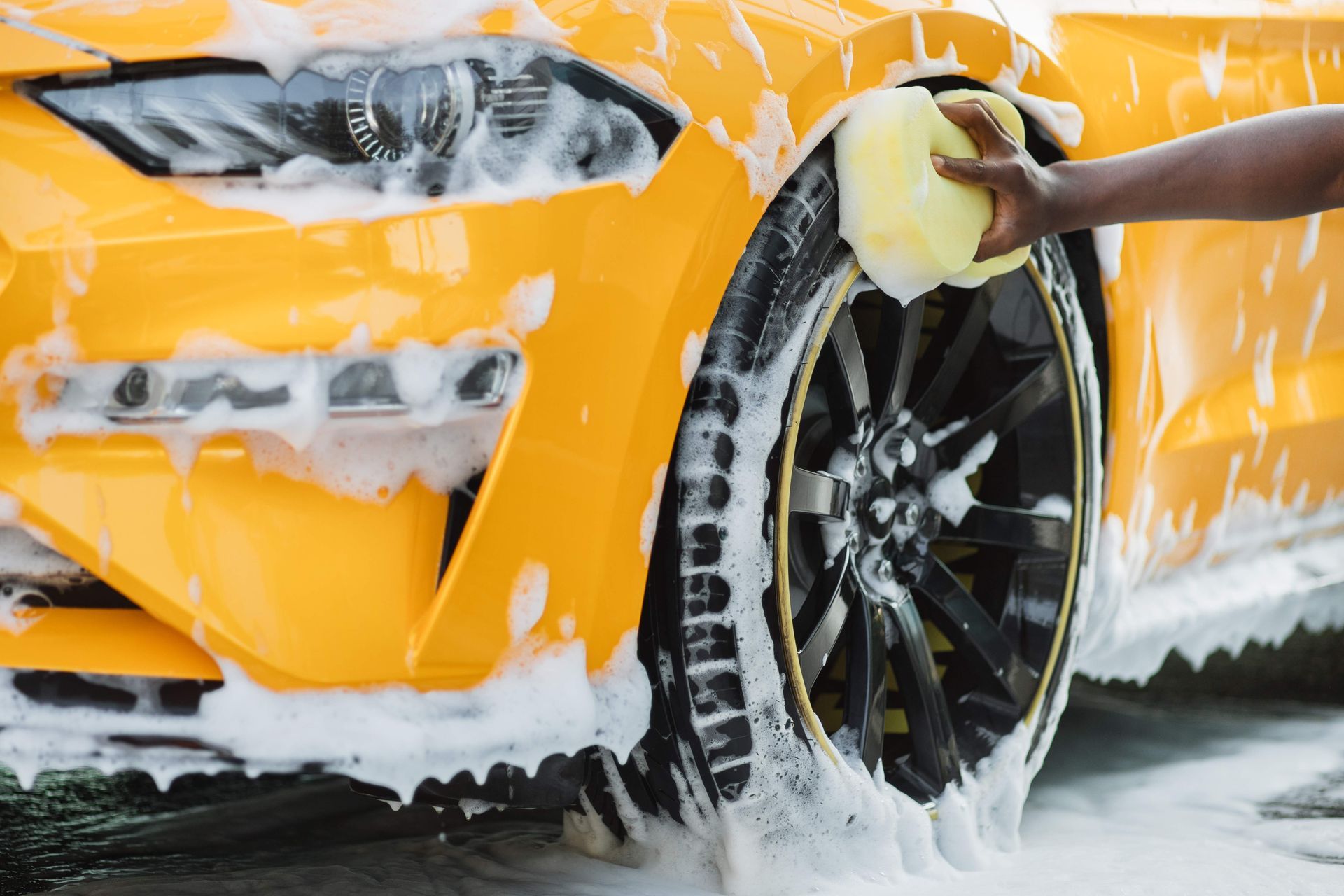 Person washing a bright yellow car tire with a soapy sponge.