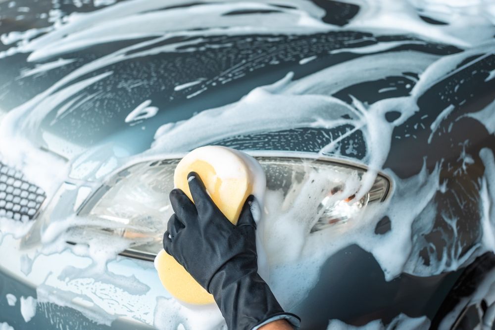 A person is washing a car with a sponge and soap.