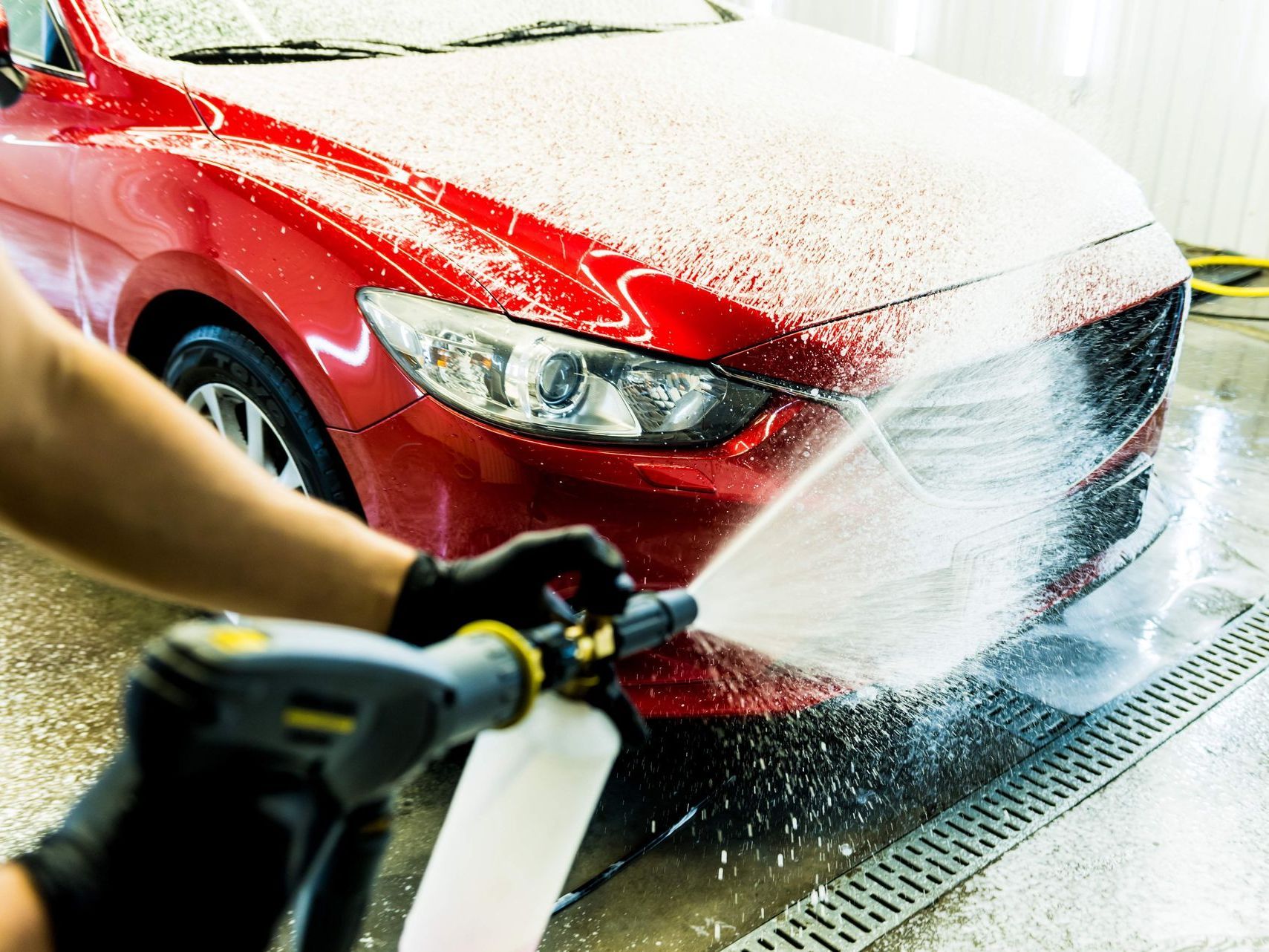 A person is washing a red car with a high pressure washer.